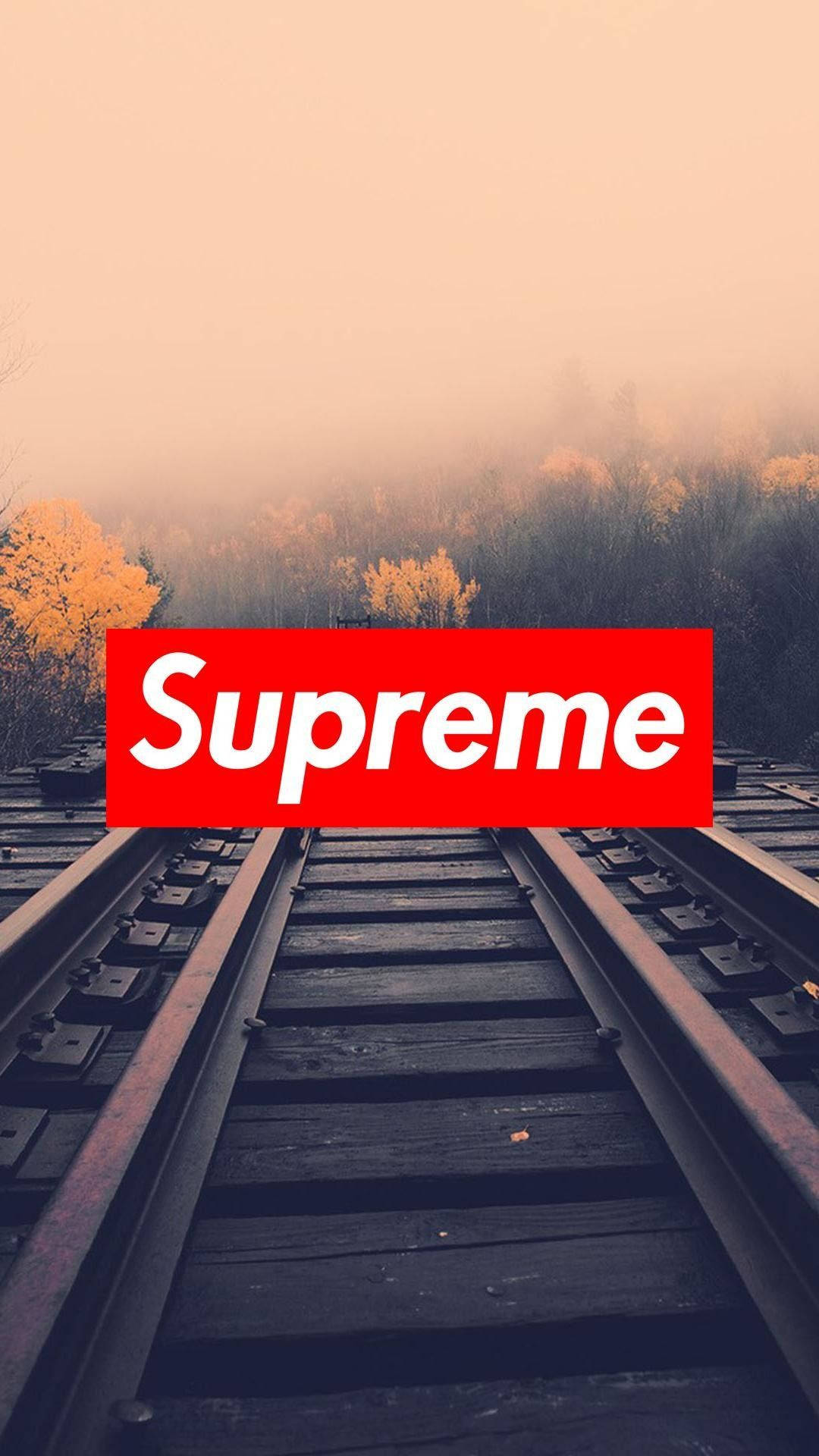Supreme標誌於山徑 壁紙 — 鐵路軌道消失在迷霧秋林中，朦朧的橙色天空下，中央有一個醒目的紅色Supreme標誌。