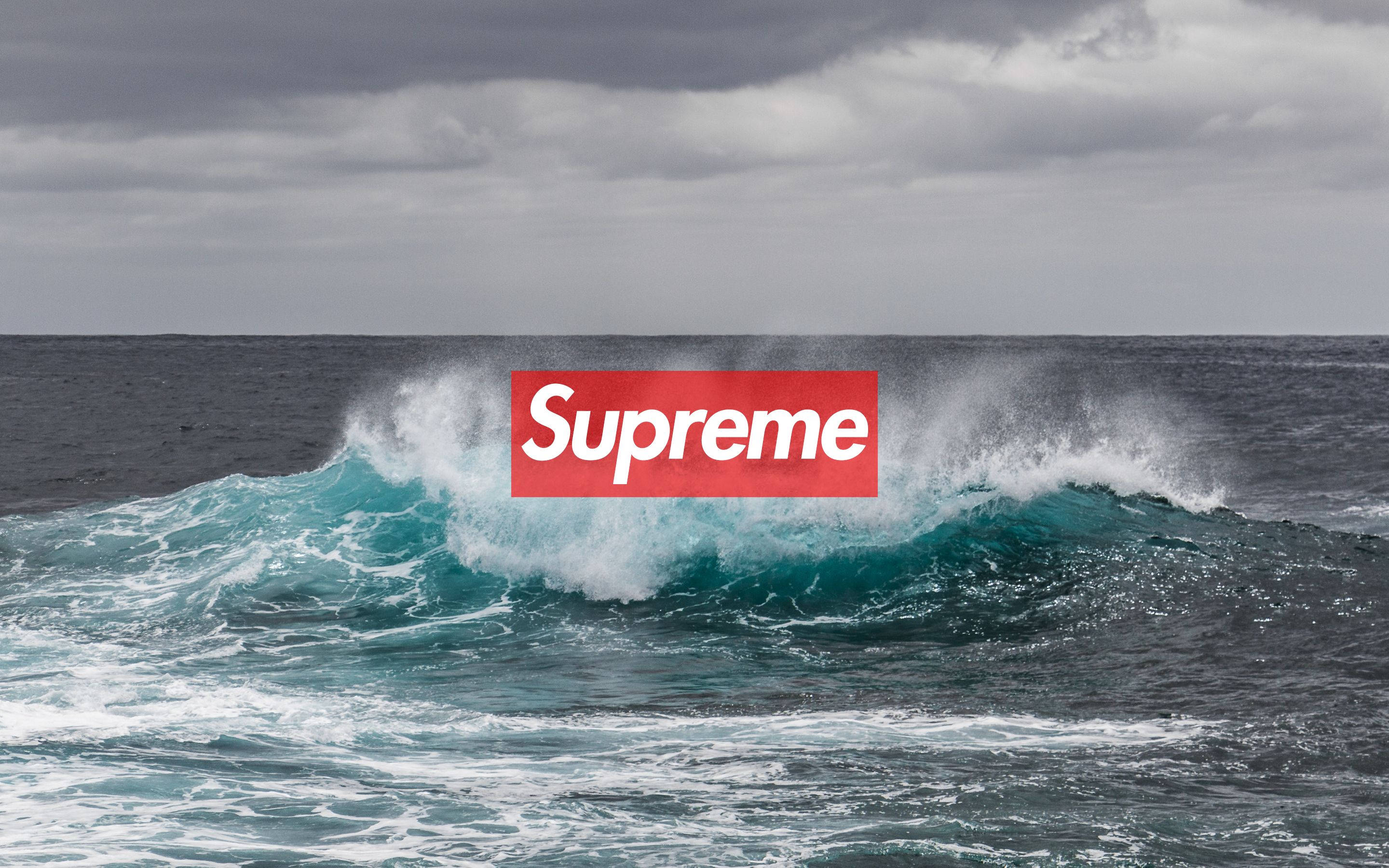 Supreme標誌於海浪 壁紙 — 在陰天天空下，一道強勁的藍綠色海浪衝擊，上面疊加了一個大膽的紅色Supreme標誌。
