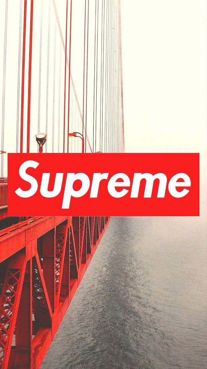 Supreme標誌於紅橋之上 壁紙 — 一個大膽的紅色Supreme標誌疊加在金門大橋的鋼結構和寧靜水面的低角度視圖上。