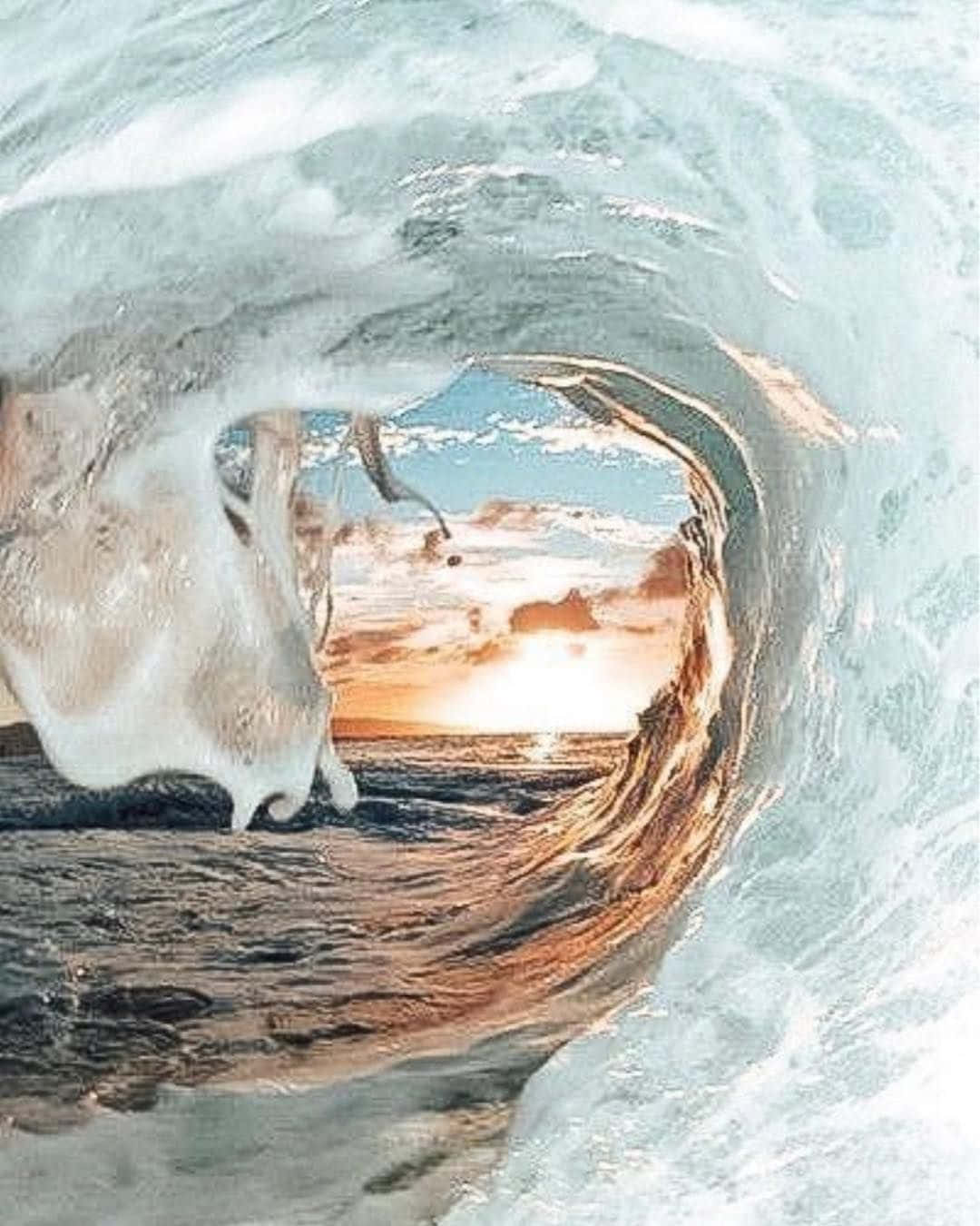  壁紙 — 一名衝浪者在捲曲的海浪隧道內滑行，金色的夕陽光線從開口處迸射而出。