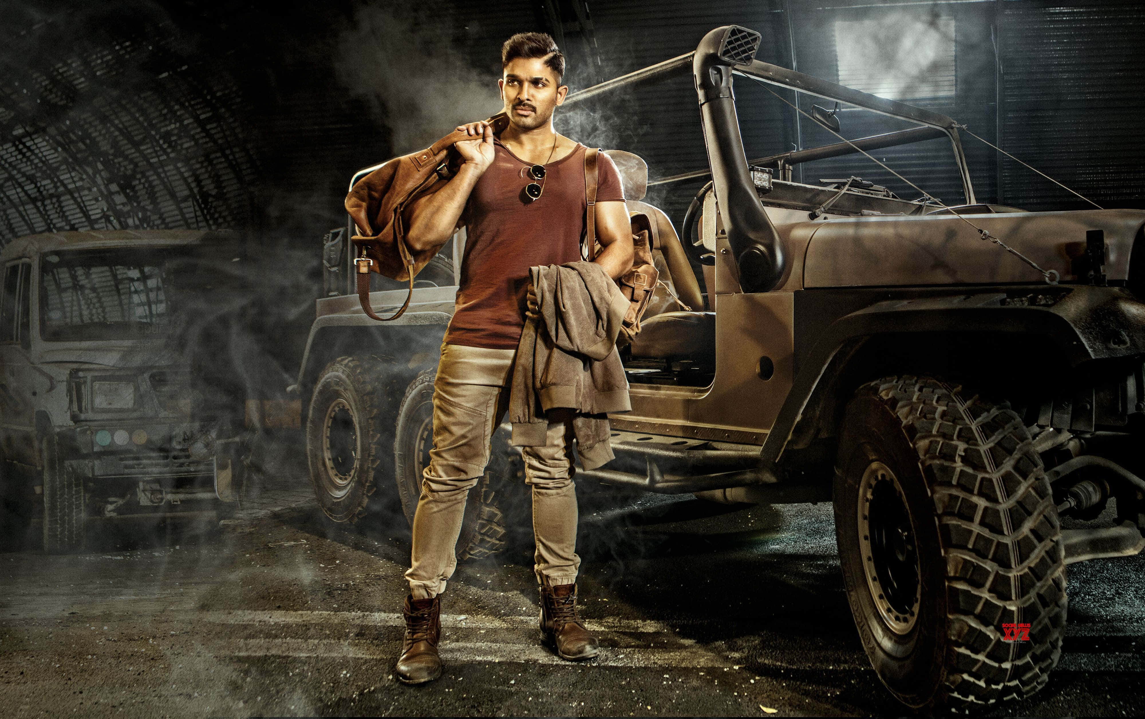 《Surya The Soldier》印度藝術家Allu Arjun 壁紙 — 一個粗獷的男人在塵土飛揚的車庫裡自信地站在一輛復古越野吉普車旁，煙霧在他周圍盤旋。