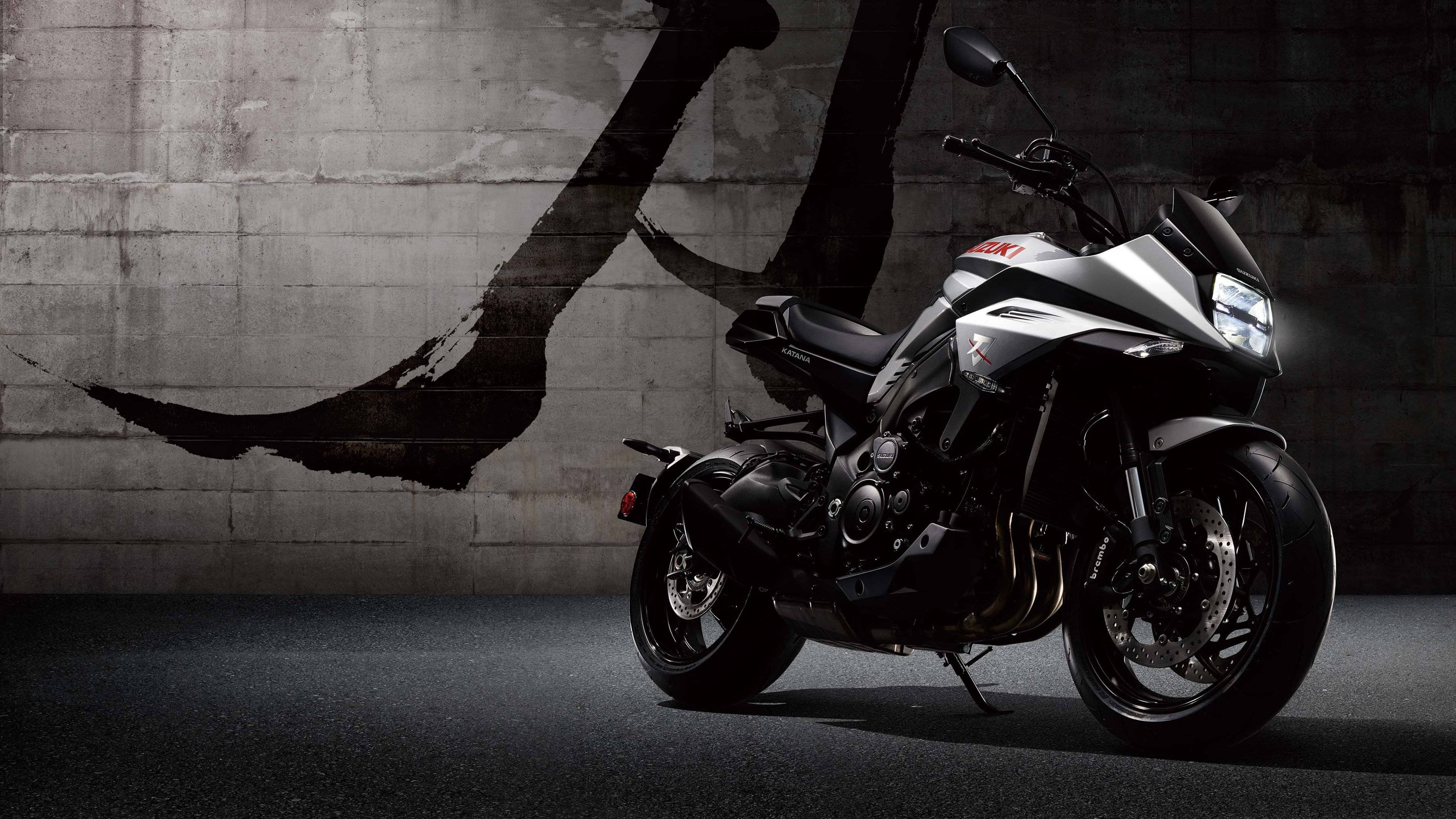 Suzuki 摩托車 壁紙 — 一架時尚的銀黑色Suzuki電單車，靠著一面飾有大膽黑色筆觸的粗糙混凝土牆。