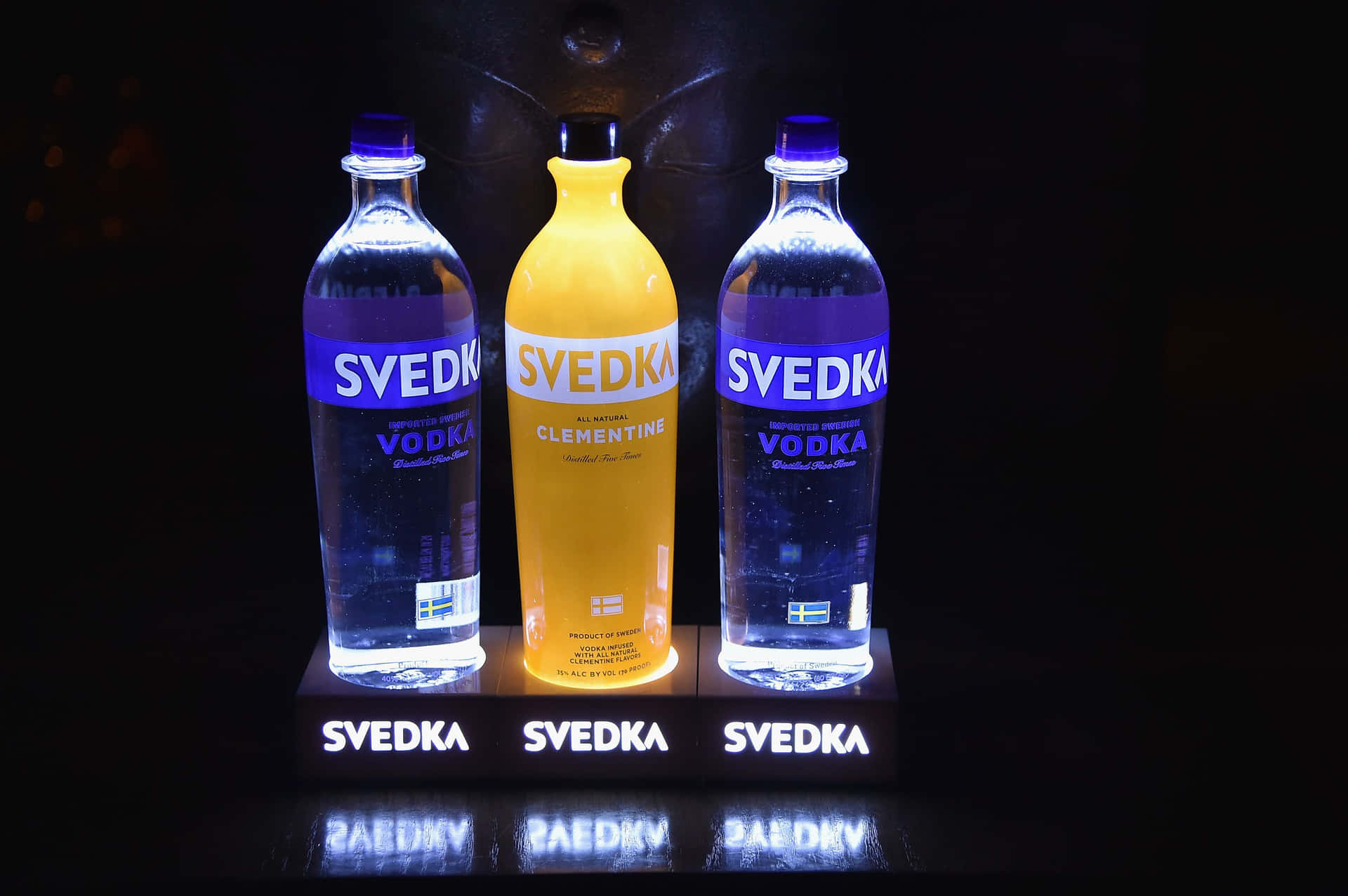 三支Svedka伏特加酒瓶在黑暗反光表面上發光。