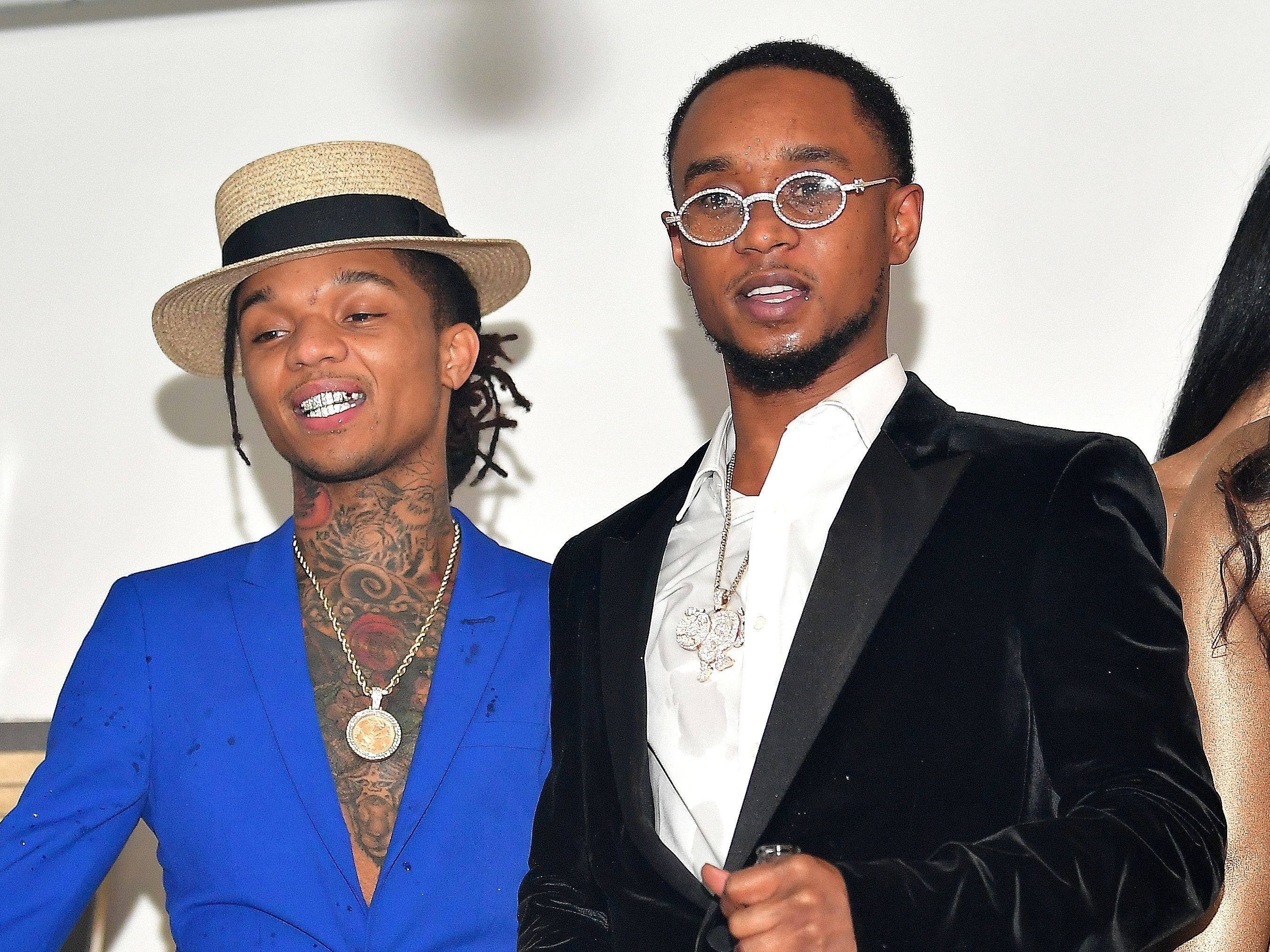Swae Lee 與另一位饒舌歌手 壁紙 — 兩位時尚男士自信地擺姿勢，一位穿著大膽的藍色西裝帶有紋身，另一位穿著黑色天鵝絨禮服配圓框眼鏡。