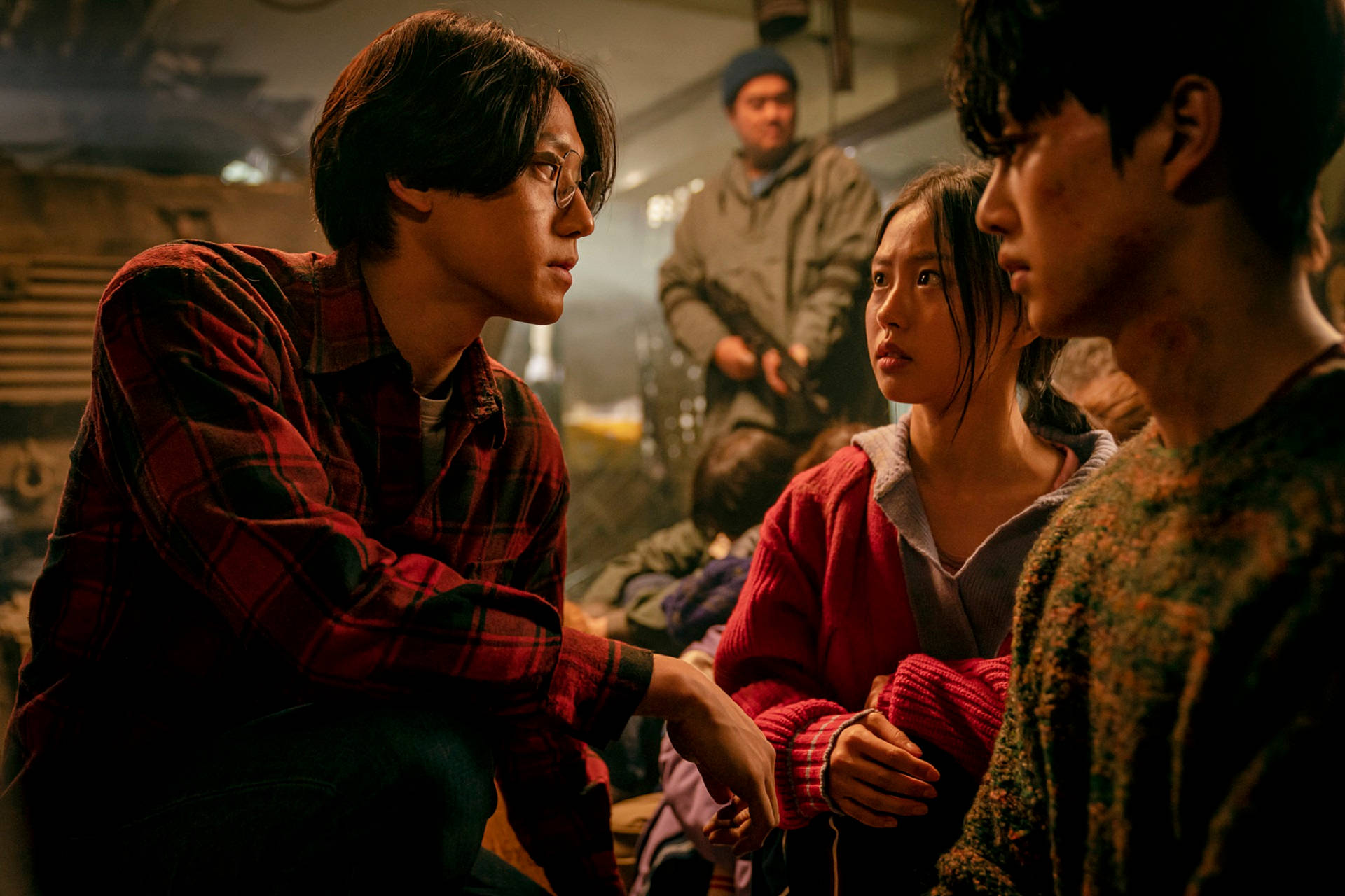 《Sweet Home》Netflix 韓劇：綠頂公寓居民集體生存 壁紙 — 三個年輕人在燈光昏暗、雜亂的房間裡，在溫暖而戲劇性的燈光下分享一個緊張而專注的時刻。