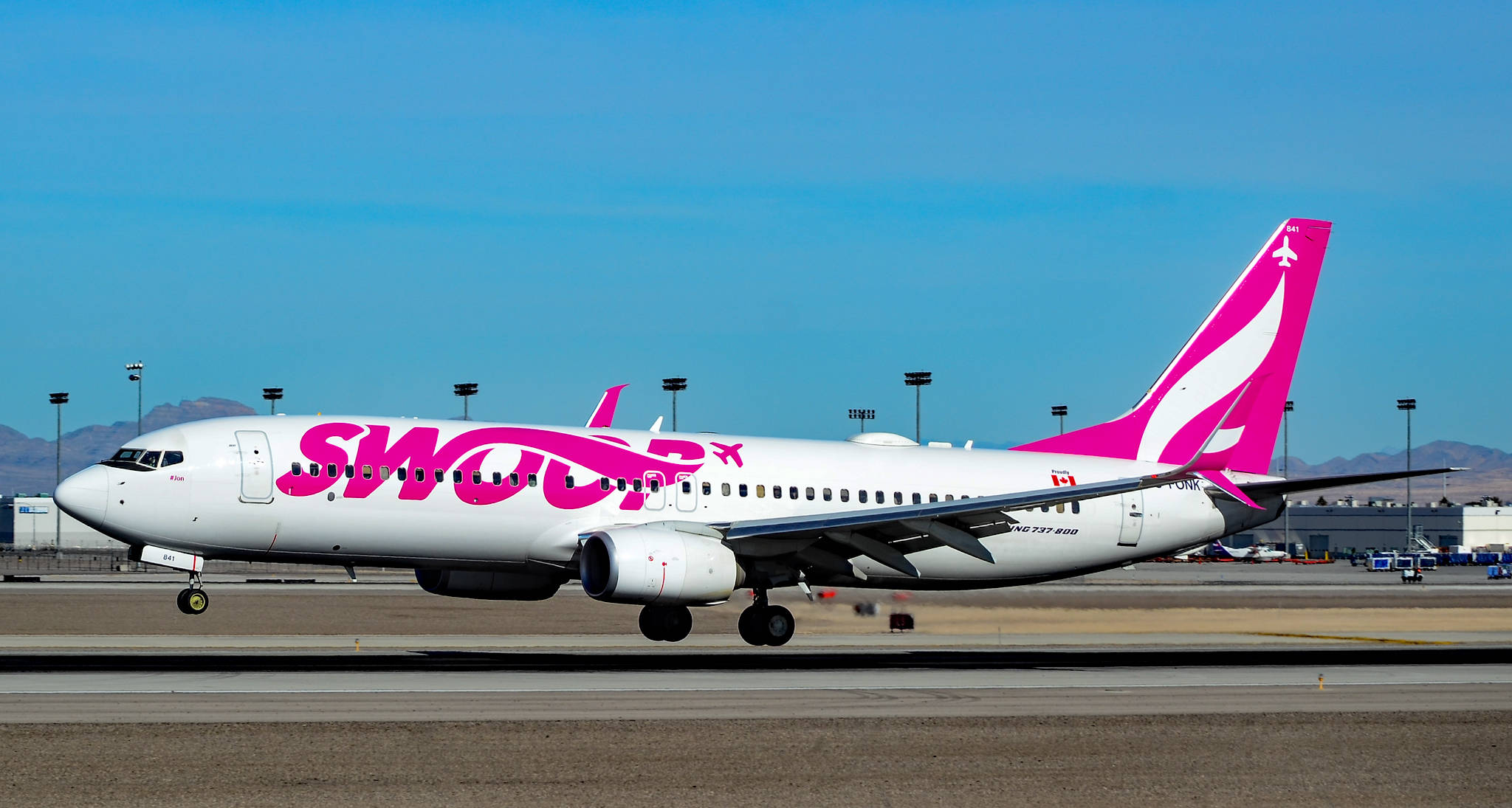 Swoop航空空中巴士在跑道 壁紙 — 一架白色Swoop飛機帶有鮮明的粉紅色品牌標誌，在晴朗藍天和遠山背景下於跑道上滑行。
