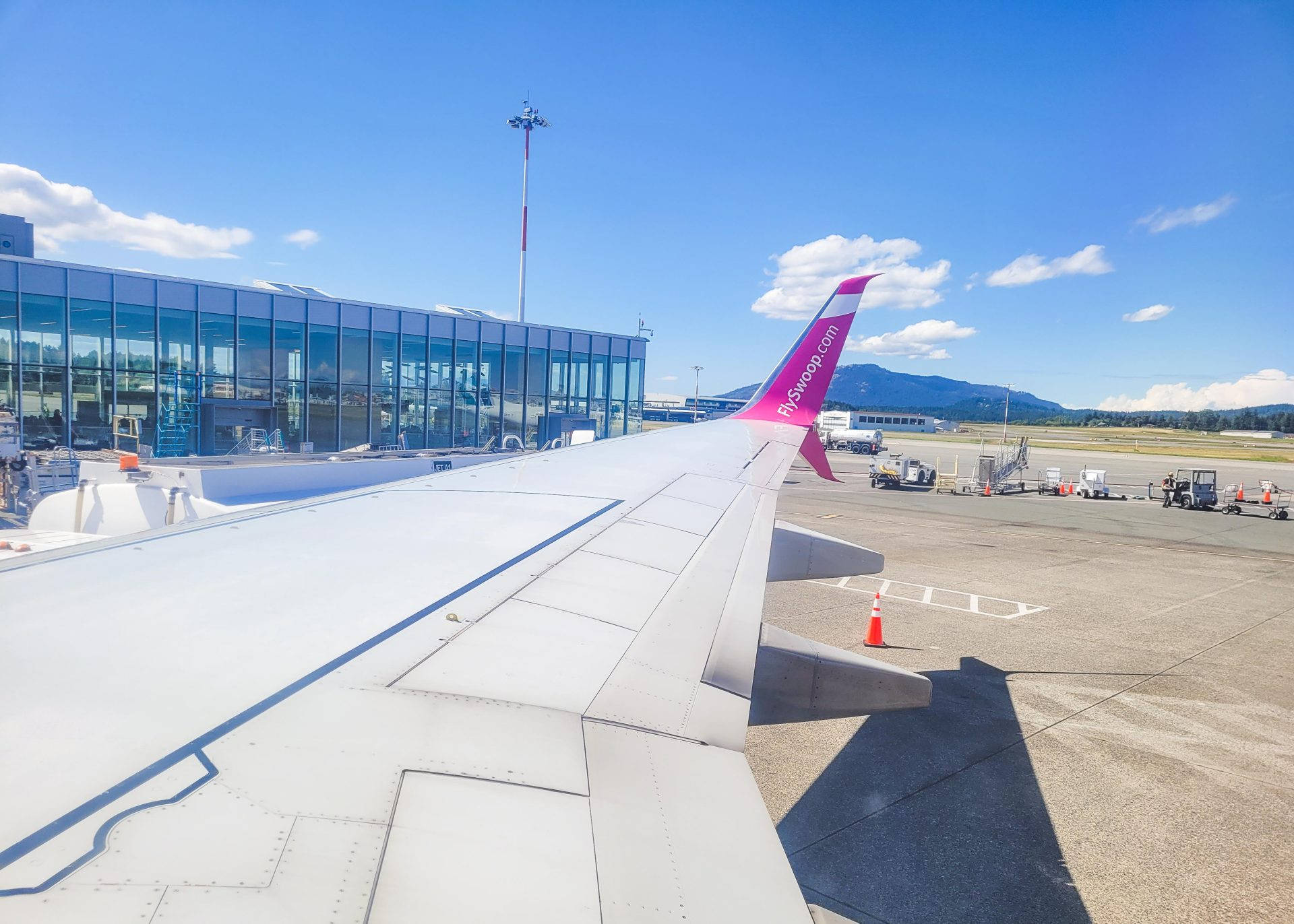 藍天下，機場客運大樓和山脈背景中的飛機機翼。
