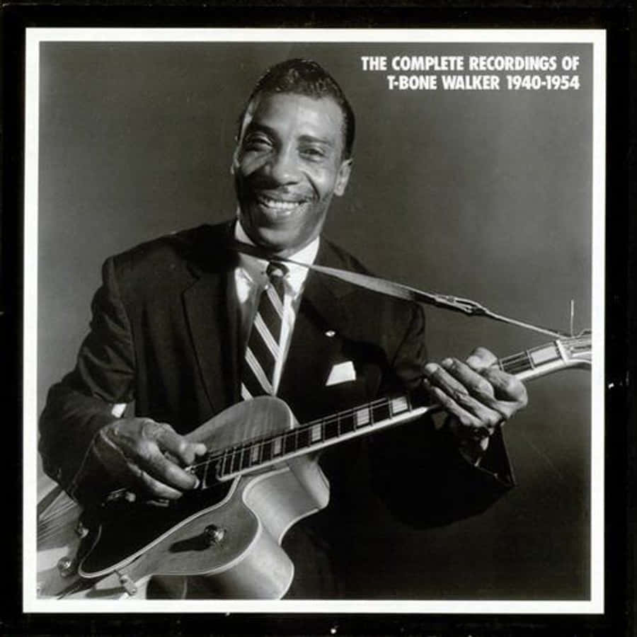 T-Bone Walker 完整錄音 壁紙 — 微笑的T-Bone Walker身穿西裝，在黑暗的攝影棚背景下手持結他，並有文字疊加。