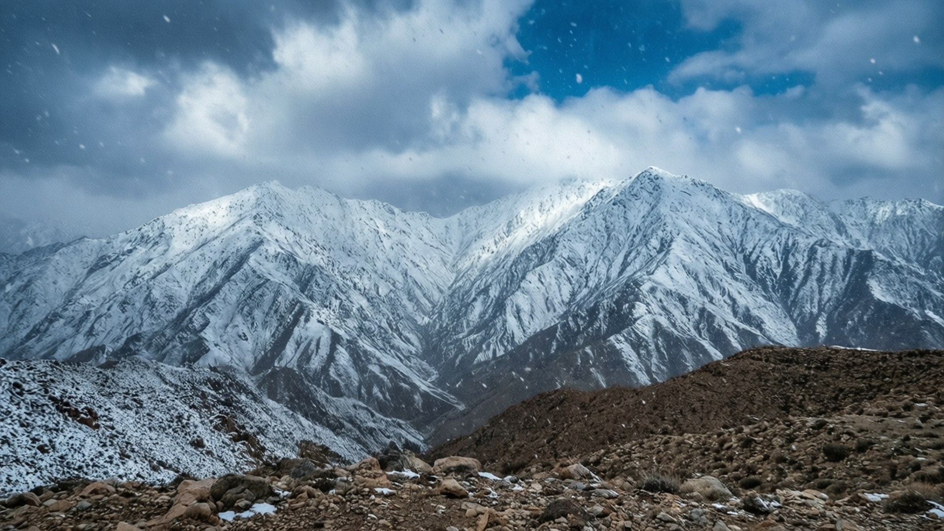 風暴天空下積雪的山脈，飄雪和岩石前景