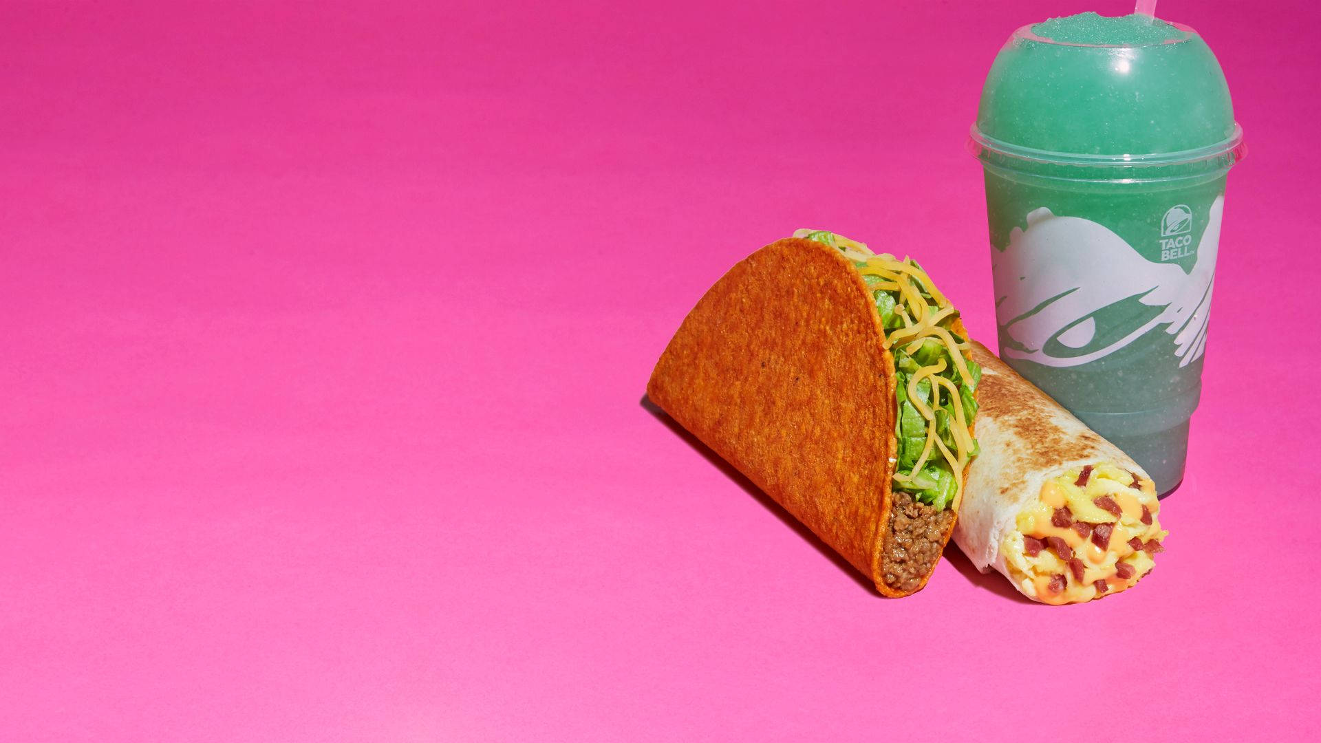Taco Bell Baja Blast飲料 壁紙 — 一個墨西哥卷餅和一個墨西哥捲餅放在一個充滿活力的粉紅色背景上，旁邊還有一杯綠色思樂冰。