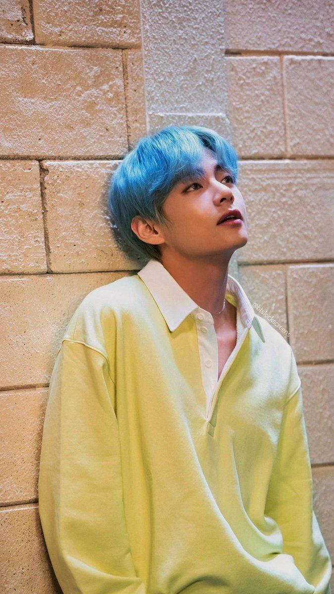 Taehyung《Lights》音樂錄影帶 壁紙 — 一位擁有鮮豔藍色頭髮的年輕男子靠著質感米色磚牆，身穿淡黃色Polo衫。
