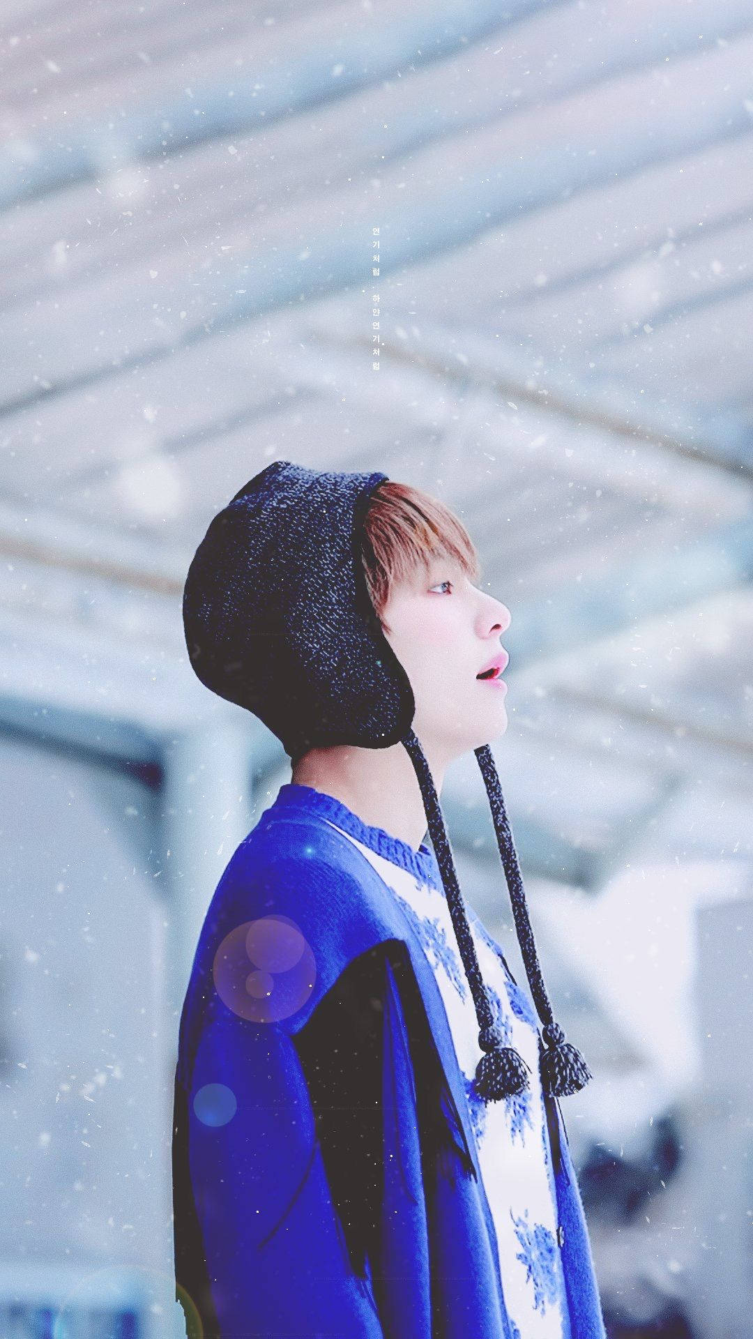 Taehyung《Spring Day》 壁紙 — 一名身穿藍色毛衣和黑色耳罩帽的年輕男子在明亮的冬日場景中仰望，雪花在他周圍飄舞。