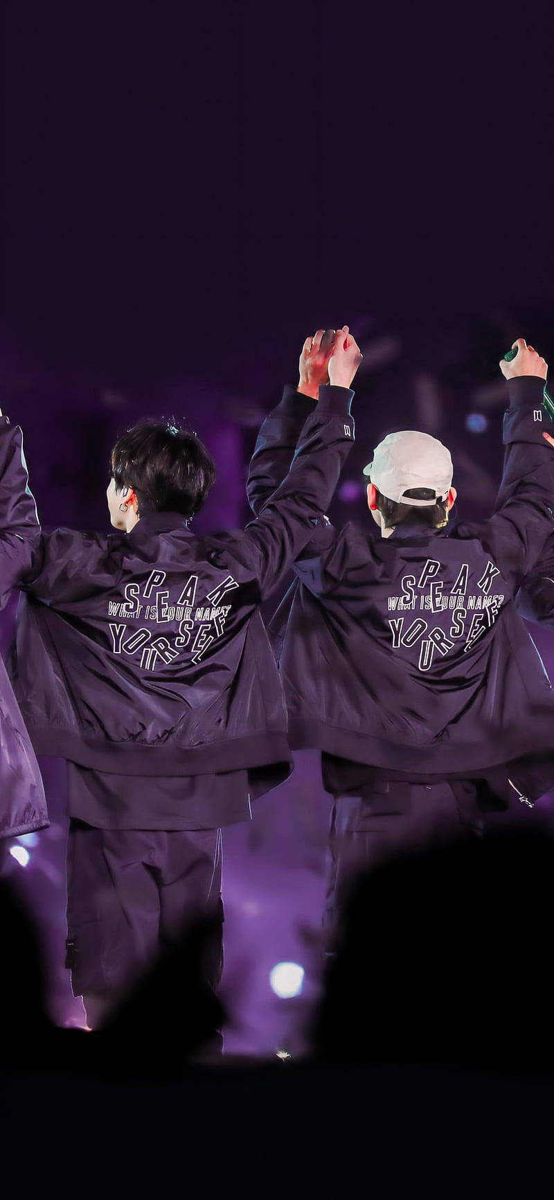 Taekook BTS Speak Yourself 夾克 壁紙 — 兩位身穿紫色外套的表演者在昏暗的舞台上，在紫色燈光下齊齊舉手。