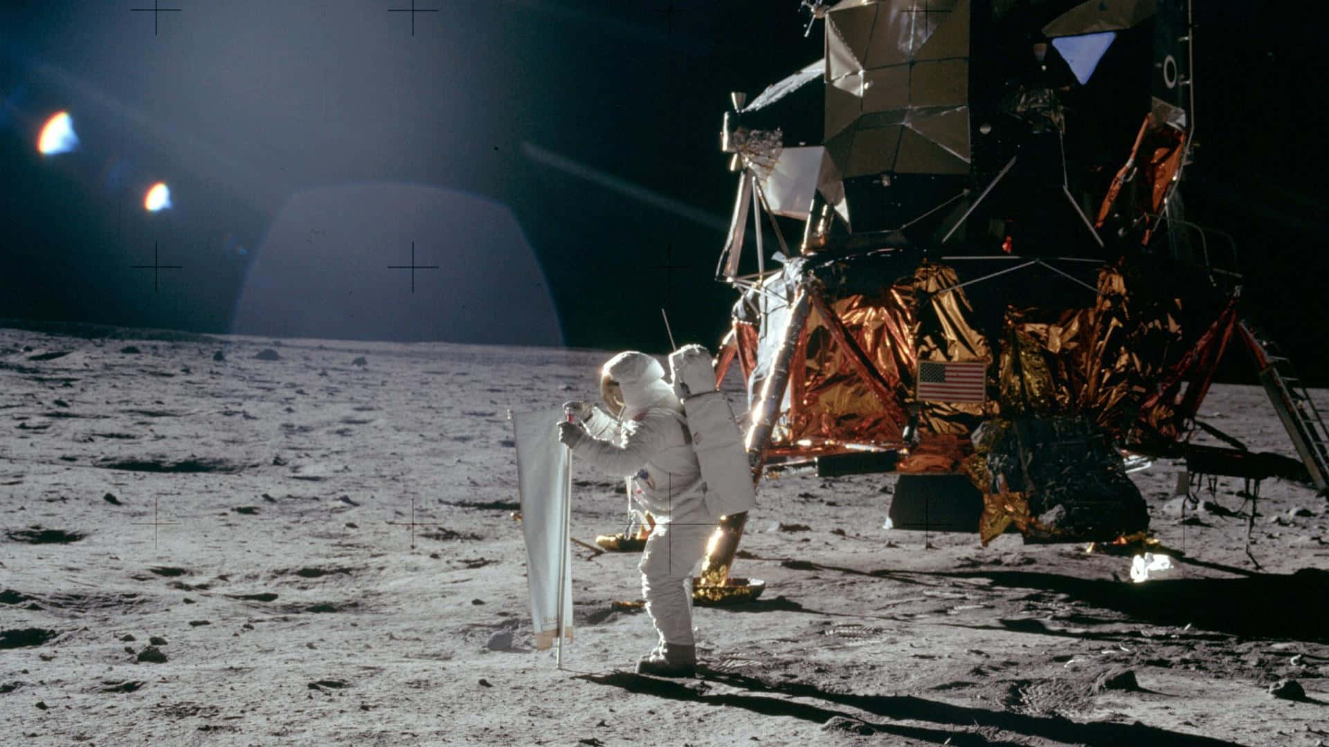 Neil Armstrong 桌布 壁紙 — 一名太空人在月球灰色表面插旗，旁邊是覆蓋金箔的登月艙，黑色天空下可見地球。