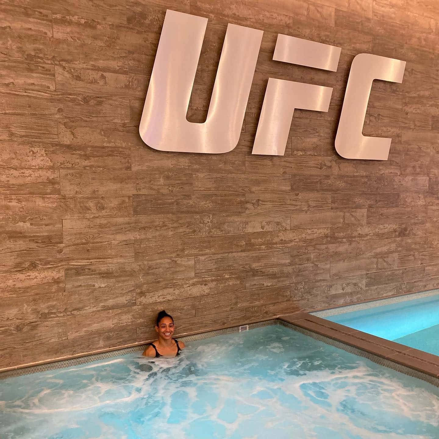 女性在木牆上UFC標誌下的熱水浴缸中微笑