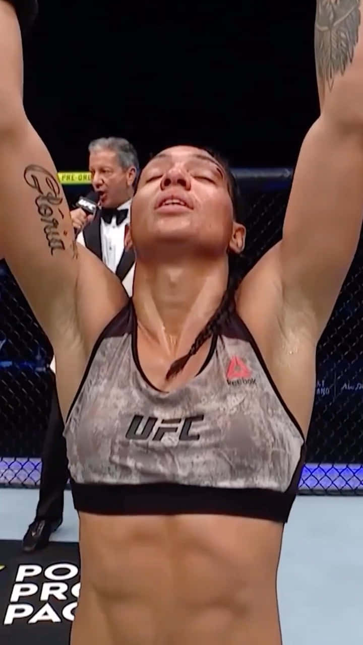 女性MMA拳手在八角籠內高舉雙臂慶祝勝利。