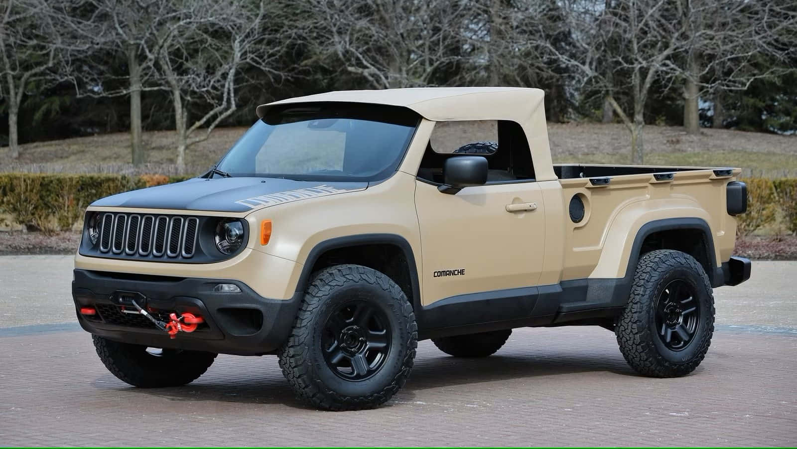 Jeep Comanche 桌布 壁紙 — 一輛棕褐色和黑色的Jeep Comanche皮卡車，配備大型越野輪胎，停泊在磚砌車道上，周圍是光禿禿的樹木。