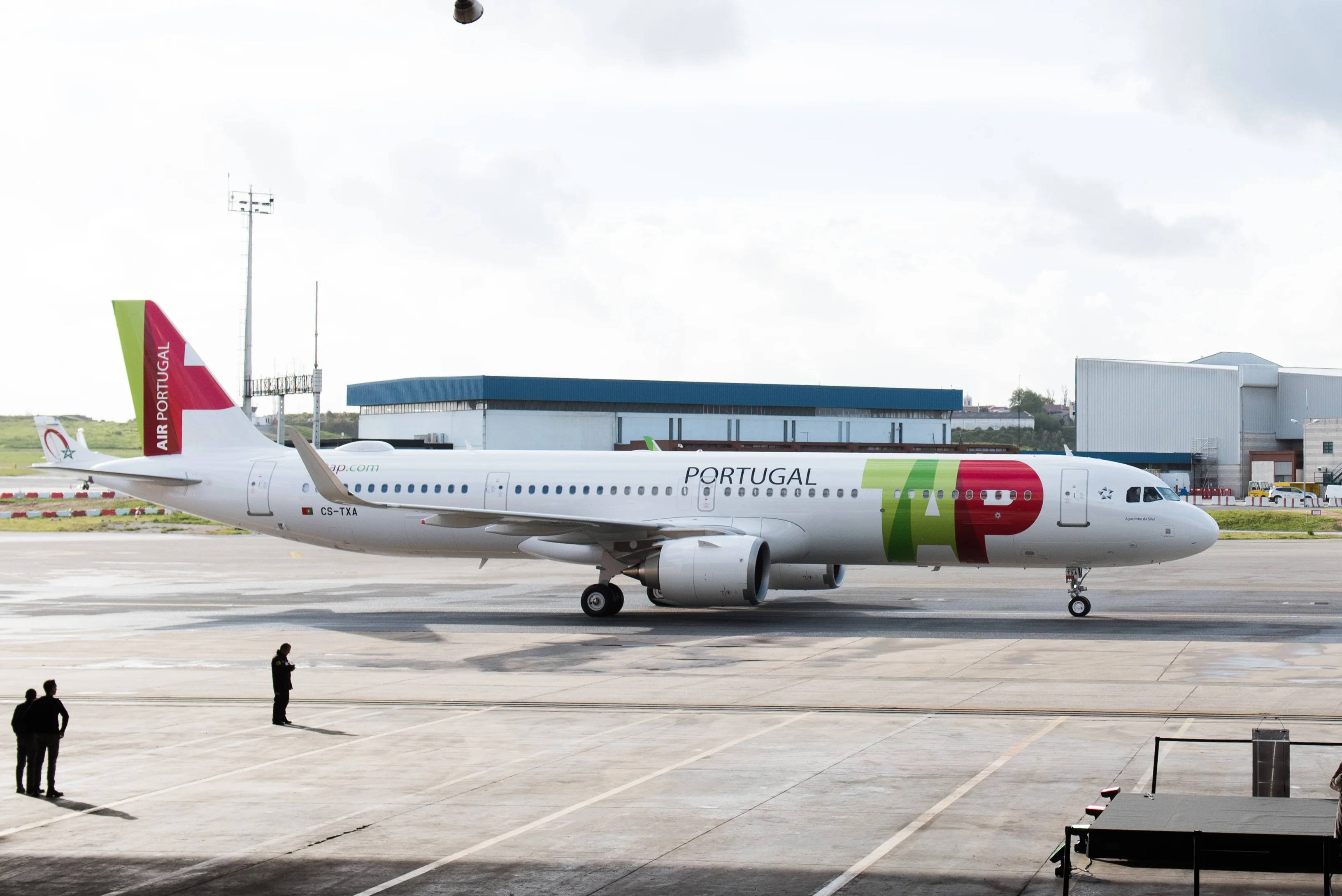 TAP葡萄牙航空機場地勤人員 壁紙 — 一架白色嘅Air Portugal空中巴士A330，帶有紅綠塗裝，喺多雲天空下喺濕滑嘅機場停機坪上滑行。