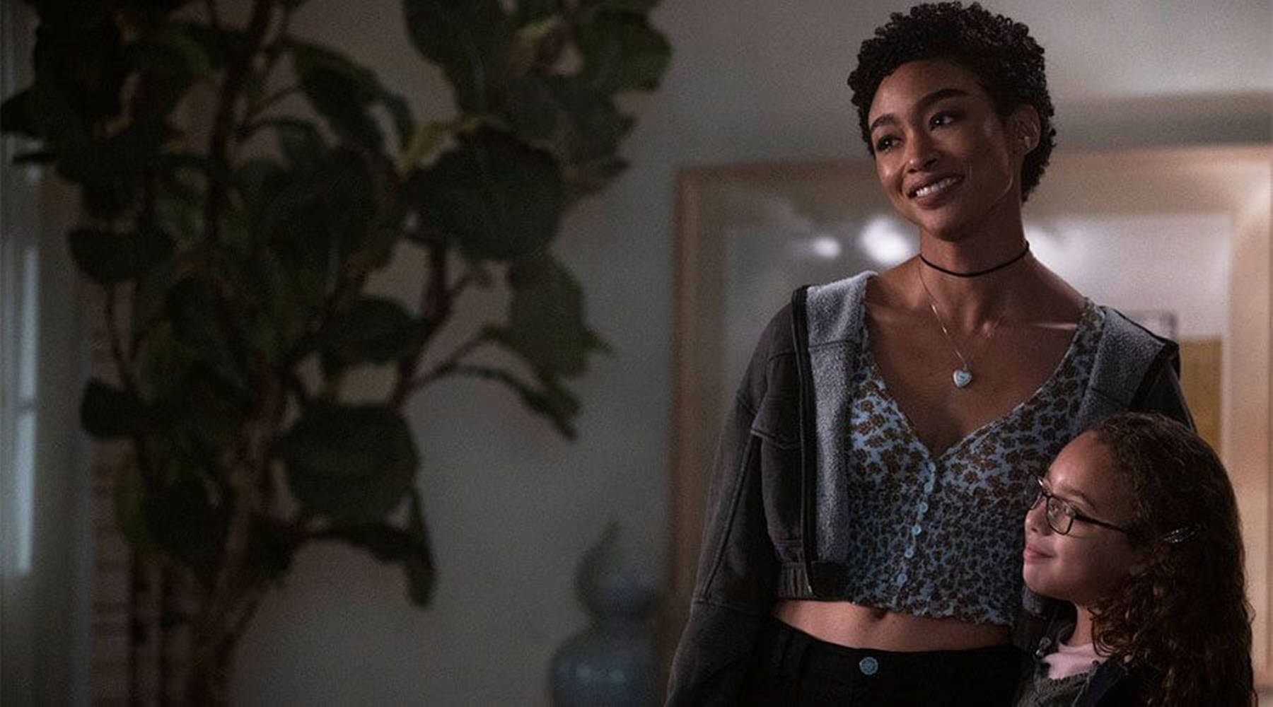 Tati Gabrielle 飾演《You》中的Marienne 壁紙 — 一個溫暖的室內場景，一位微笑的女性穿著豹紋短版上衣，一個戴眼鏡的小女孩抬頭看著她。