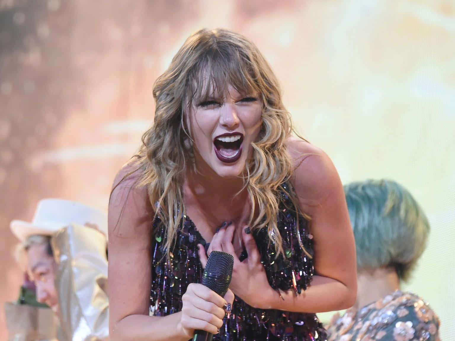 Taylor Swift Lover 桌布 壁紙 — Taylor Swift 熱情地對著咪高峰唱歌，身穿閃亮黑色連衣裙，金色頭髮。