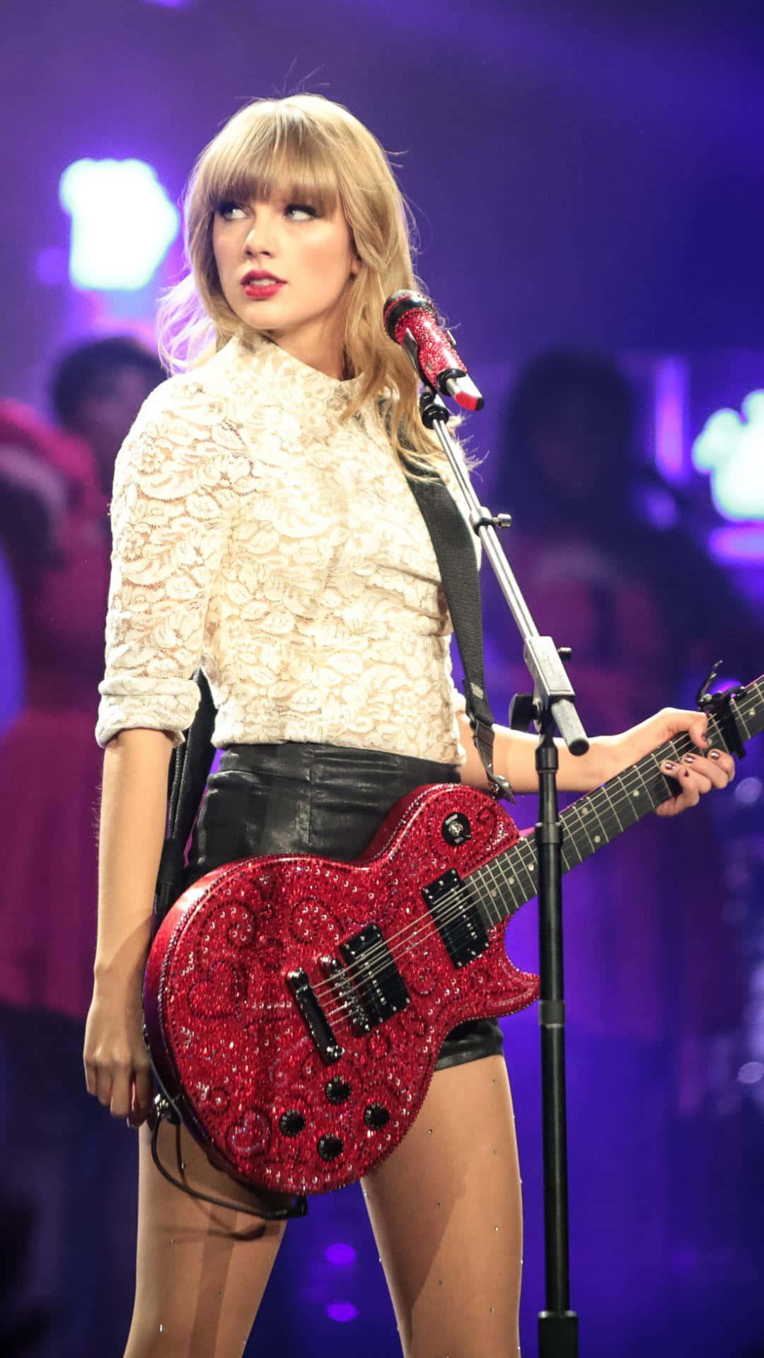 Taylor Swift Lover 桌布 壁紙 — Taylor Swift 在紫色舞台燈光下手持閃亮紅色電結他表演。