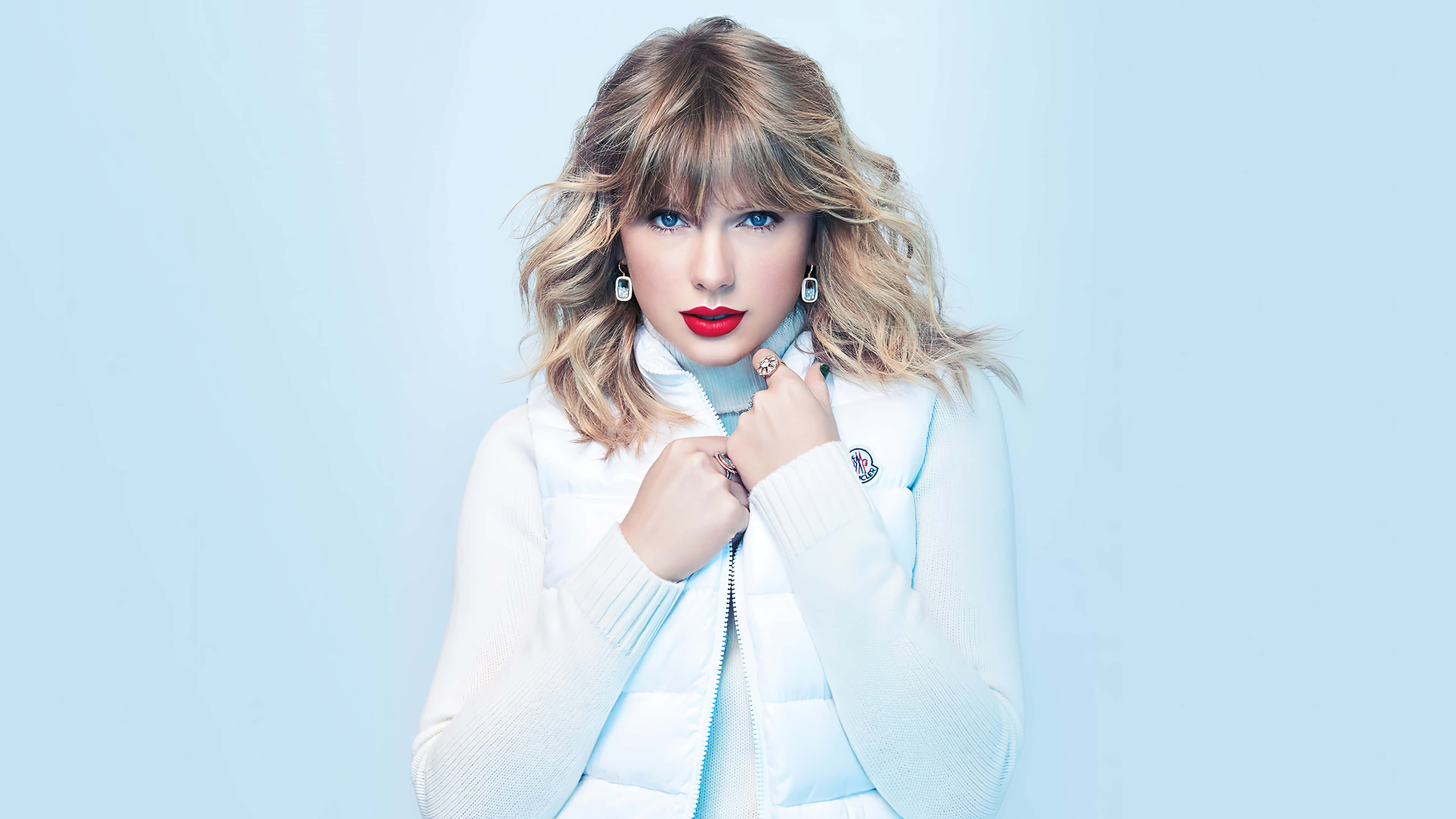 Taylor Swift 桌布 壁紙 — Taylor Swift 喺柔和藍色嘅工作室背景前，自信咁擺出姿勢，著住一件白色羽絨外套。