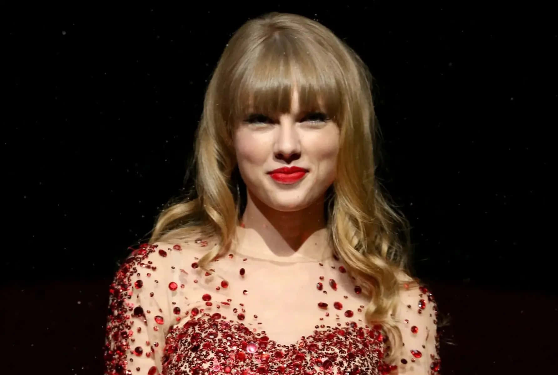 Taylor Swift 桌布 壁紙 — Taylor Swift 穿著閃亮的紅色亮片連衣裙，在黑暗的星空背景下微笑。
