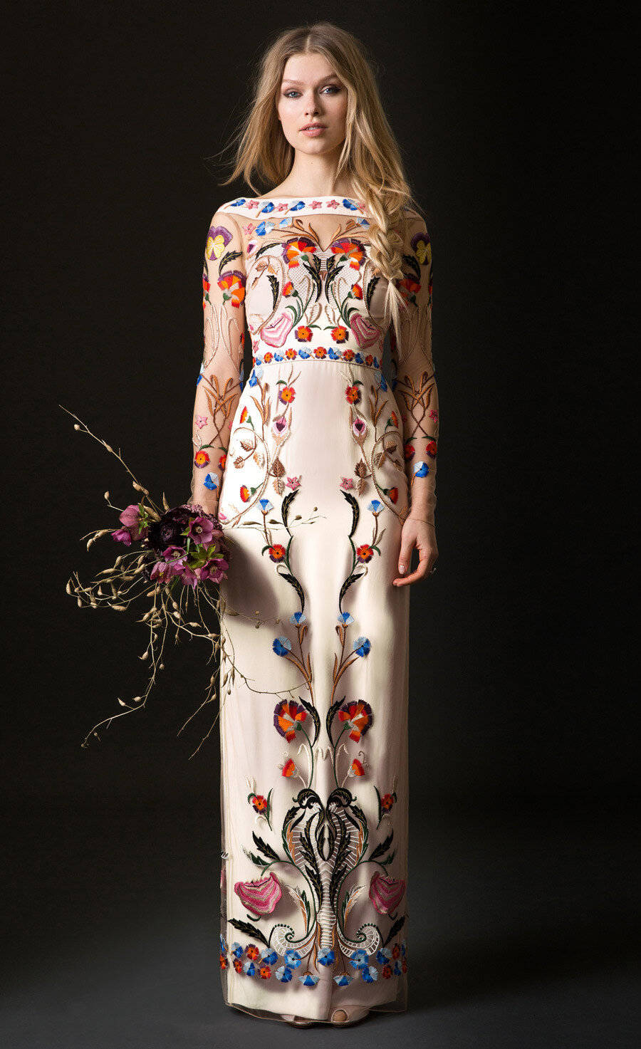 身穿花卉刺繡禮服的女士在黑暗攝影棚中手持花束。