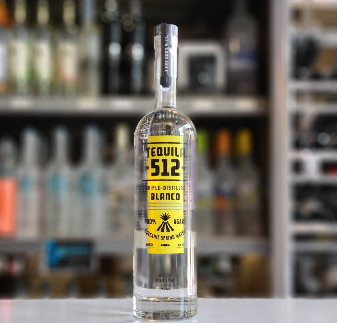 Tequila 512 Blanco 瓶身搭配模糊酒吧背景 壁紙 — 一瓶透明的Tequila 512 Blanco，帶有鮮明的黃色標籤，放在吧檯中央，背景是柔和模糊的酒架。