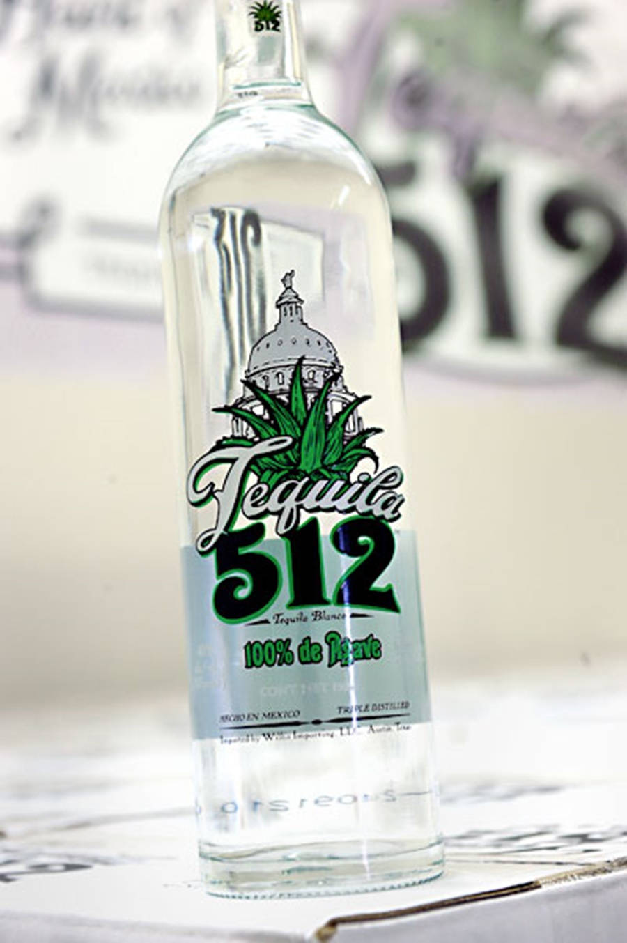 Tequila 512 瓶身於樸素背景 壁紙 — 一瓶清晰玻璃瓶裝的Tequila 512，帶有綠色標籤和龍舌蘭植物圖案，在模糊背景中清晰對焦。