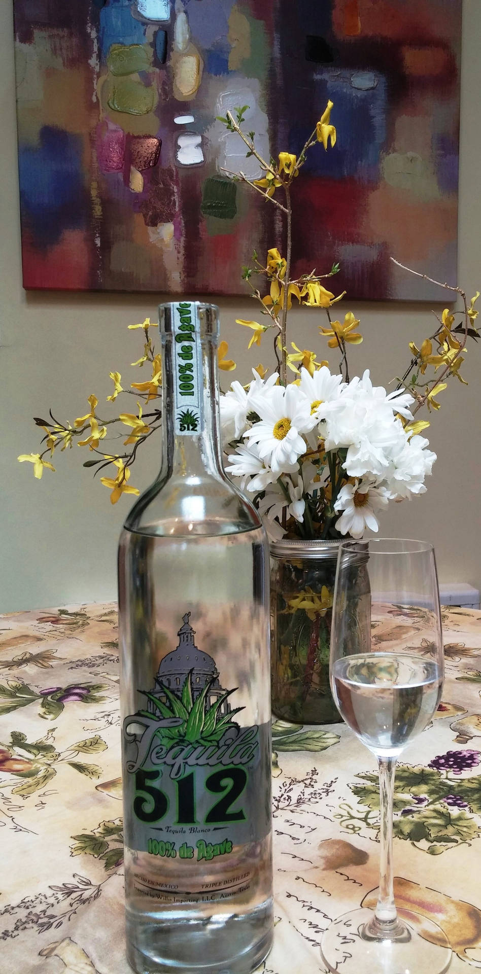 室內花卉桌布上的龍舌蘭酒瓶、酒杯和鮮花。