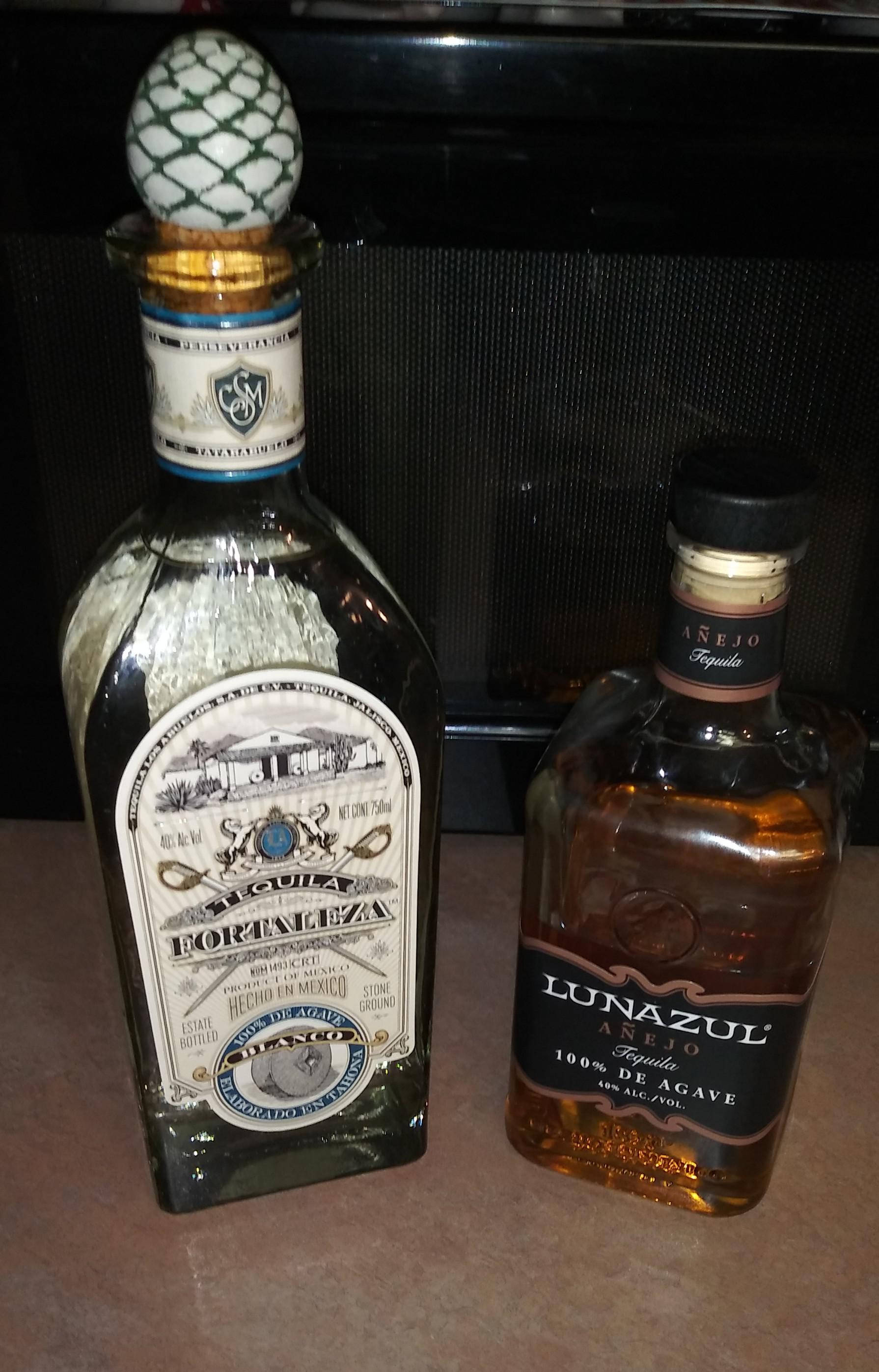 Tequila Fortaleza Blanco與Lunazul Anejo龍舌蘭酒 壁紙 — 兩個不同的龍舌蘭酒瓶，一個帶有菠蘿塞和華麗標籤，另一個帶有琥珀色液體和時尚黑色瓶蓋，並排放在枱面上。