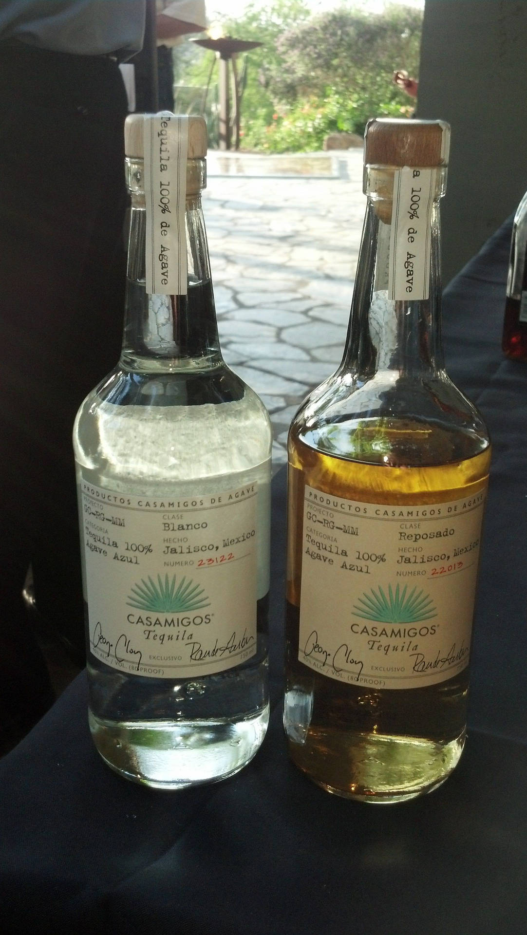 兩瓶Casamigos龍舌蘭酒blanco和reposado放在戶外深色桌子上。