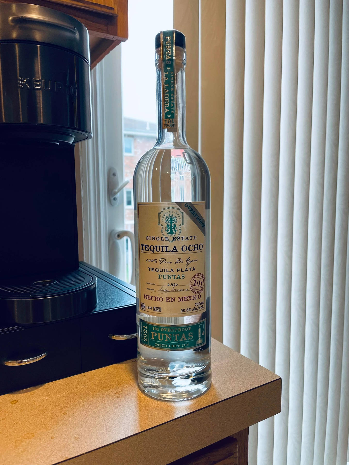 廚房枱面上的透明龍舌蘭酒瓶，旁邊有咖啡機和百葉簾。