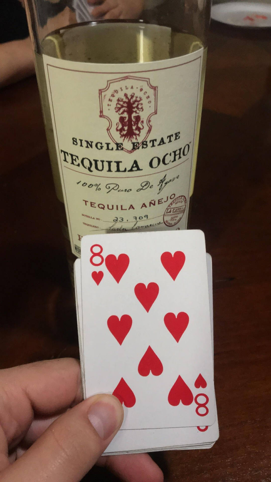 手拿紅心8牌靠近龍舌蘭酒瓶在木桌上