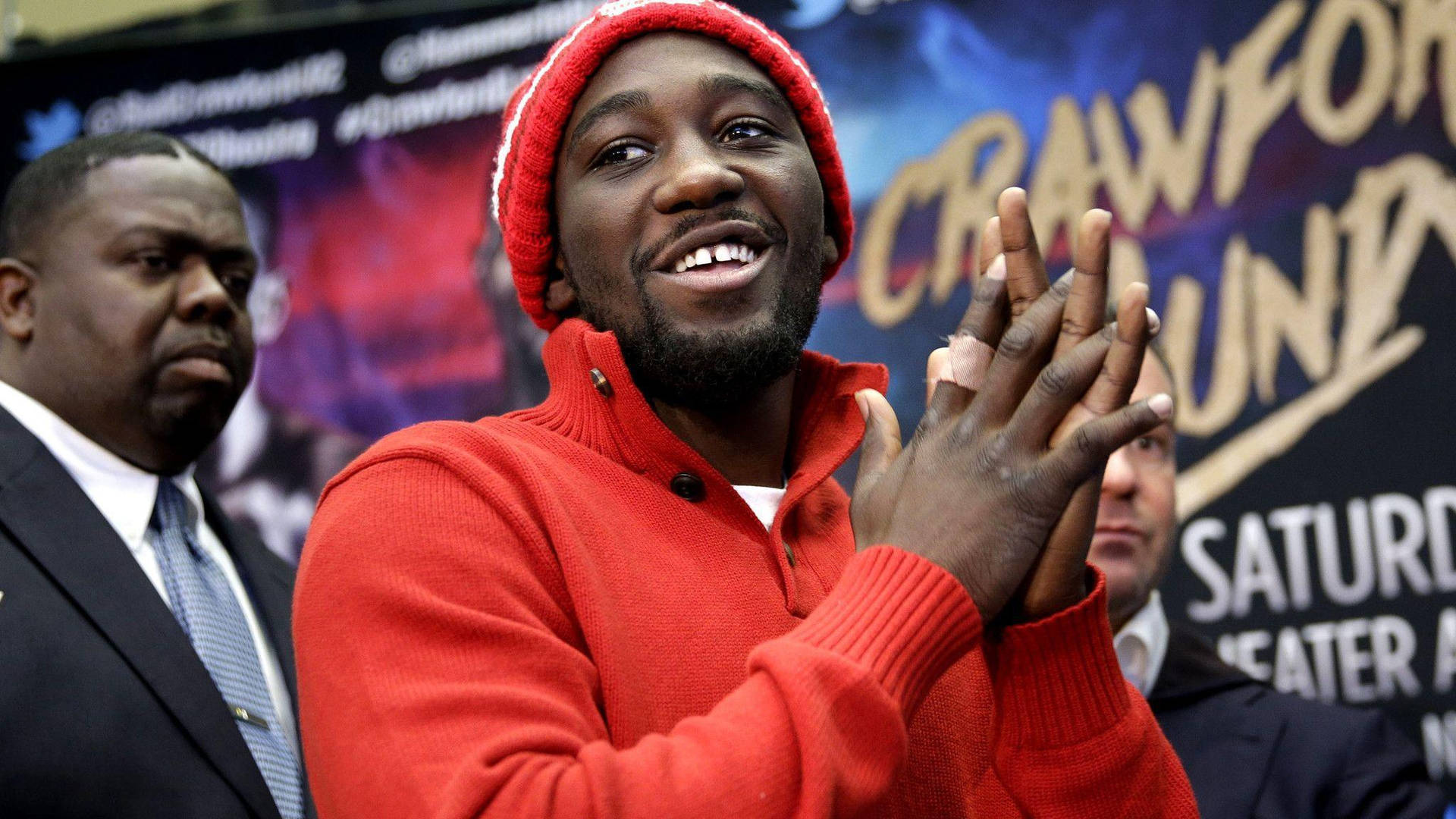 Terence Crawford 鼓掌 壁紙 — 一位戴紅色冷帽、穿紅色毛衣的男士在拳擊活動記者會上熱情鼓掌。