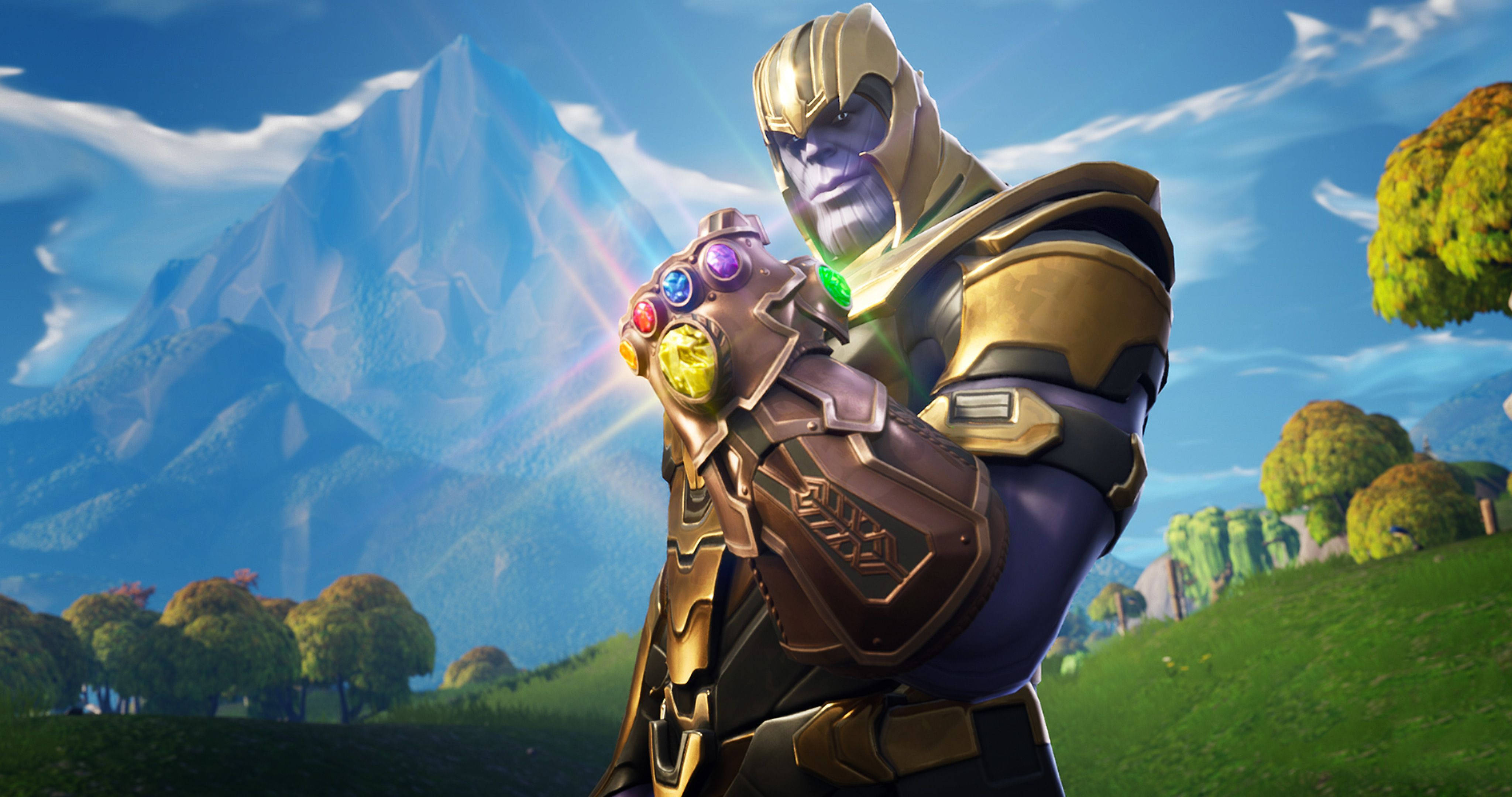 Fortnite 桌布 壁紙 — Thanos 站在充滿活力的田野中，手持發光的無限手套，背景是白雪覆蓋的山脈和藍天。
