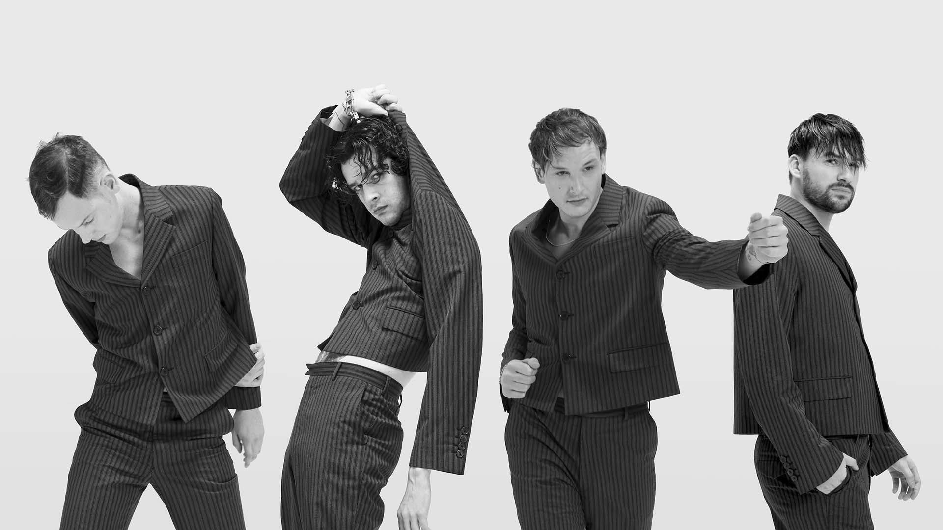 The 1975 條紋正裝造型 壁紙 — 四位身穿細條紋西裝的男士在單色工作室拍攝中，以純灰色背景擺出動態姿勢。