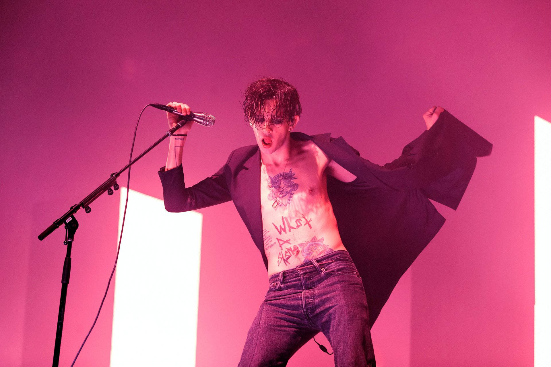 The 1975 馬修·希利激情演出 壁紙 — 一位赤裸上身、帶有紋身和眼鏡的表演者在強烈的粉紅色舞台燈光下，熱情地對著麥克風唱歌。