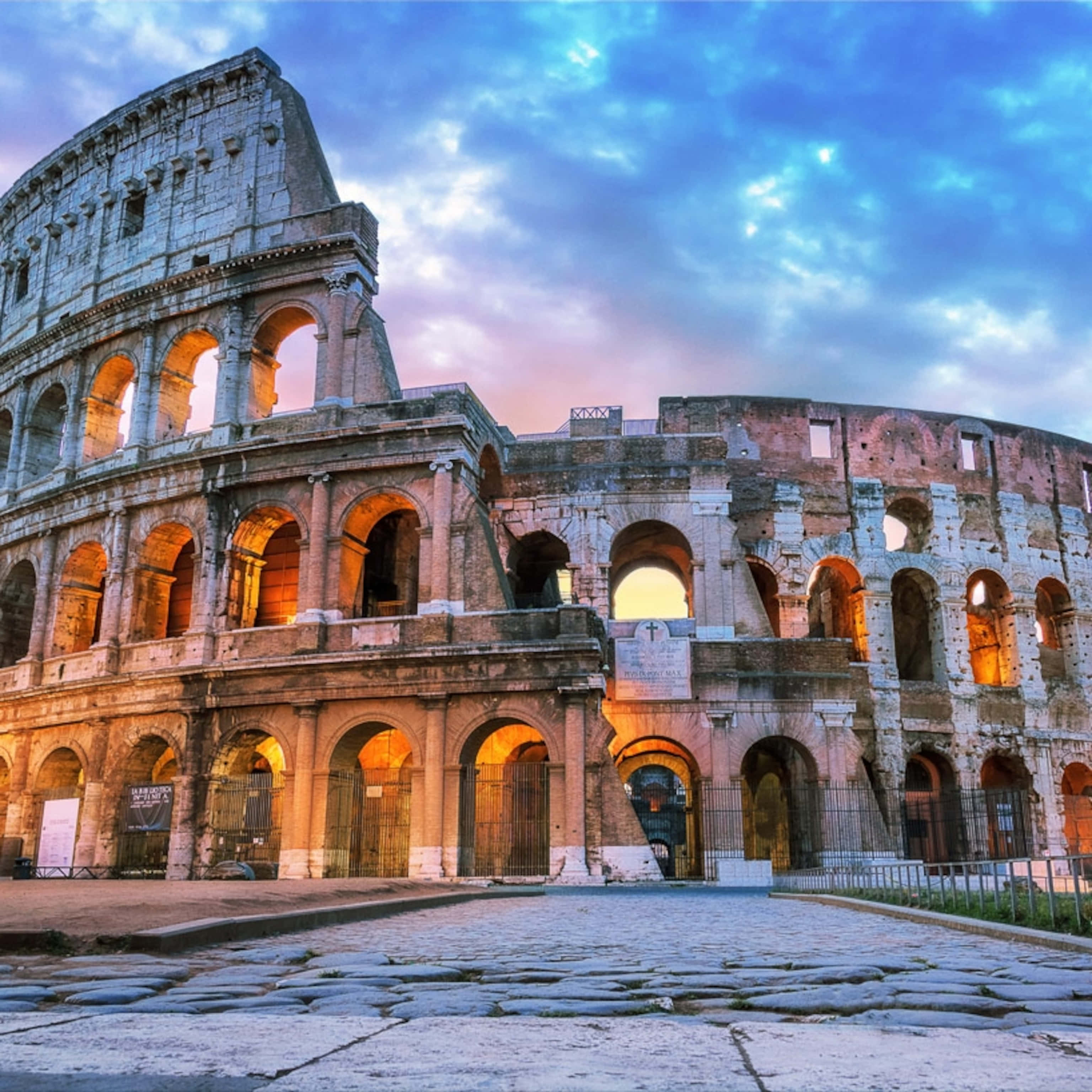 Roman 桌布 壁紙 — 古老的羅馬鬥獸場在暮色天空下巍然聳立，溫暖的室內燈光透過拱門閃爍。
