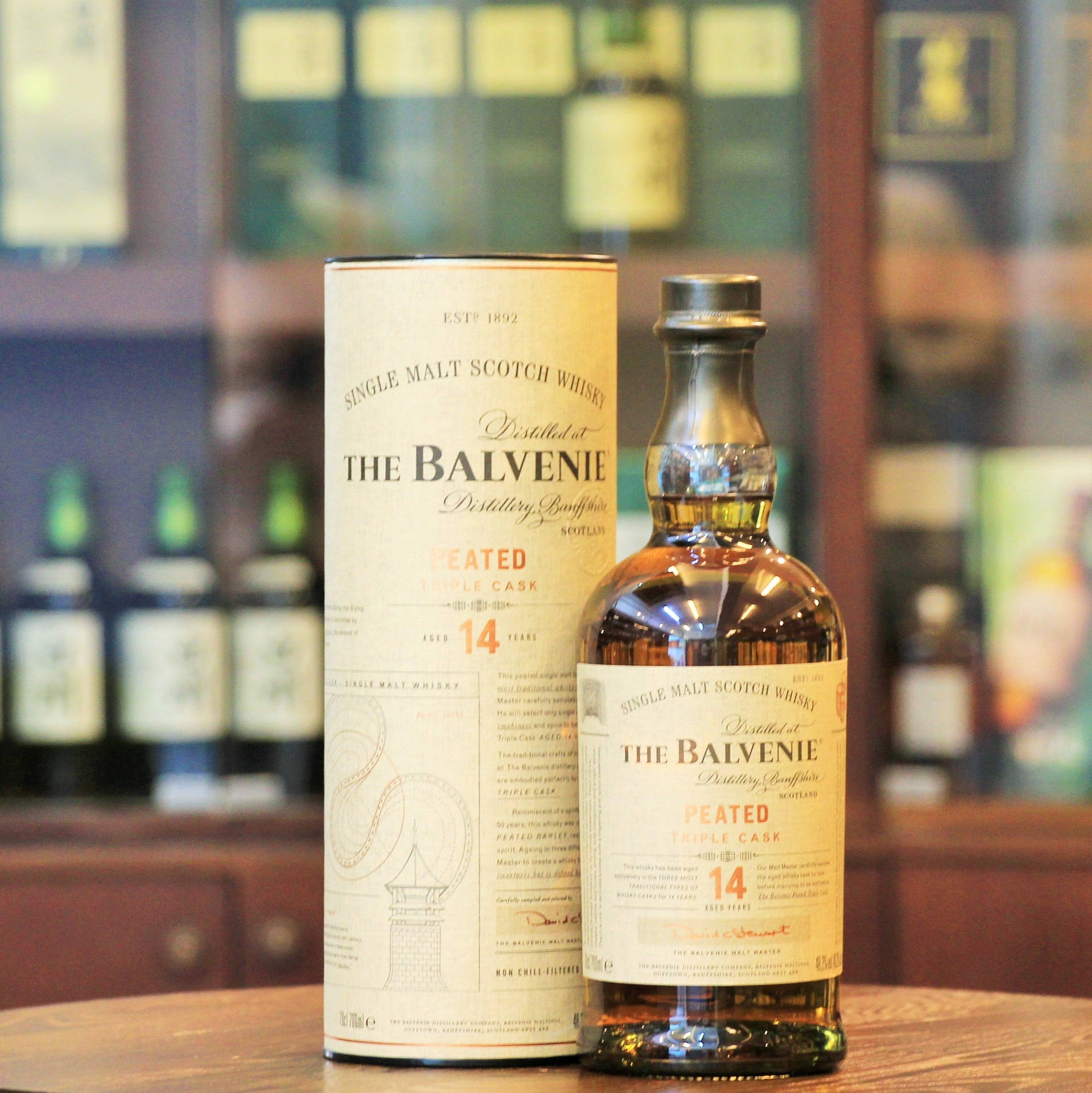 木製吧檯上的一瓶及一盒Balvenie 14年泥煤威士忌。