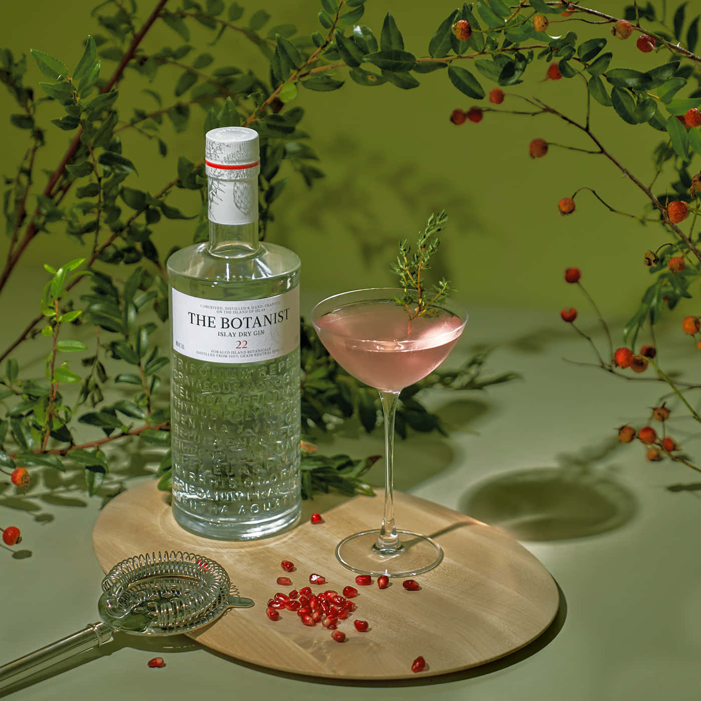 Botanist 氈酒瓶和粉紅色雞尾酒，配以香草和石榴籽，放在木板上。