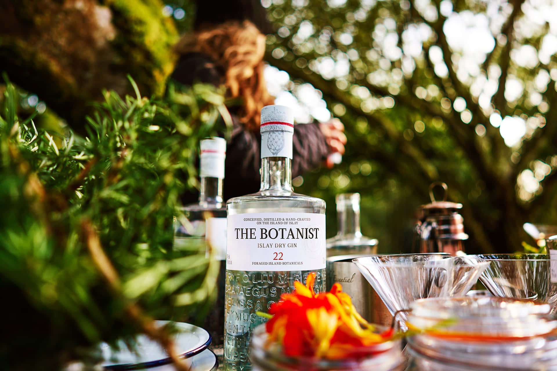 花園日落時分，桌上放著 The Botanist 氈酒、香草和杯子。