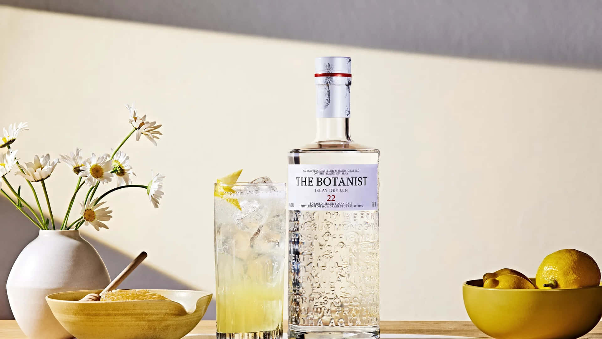 Botanist 氈酒瓶，配以雞尾酒和雛菊，在溫暖光線中。