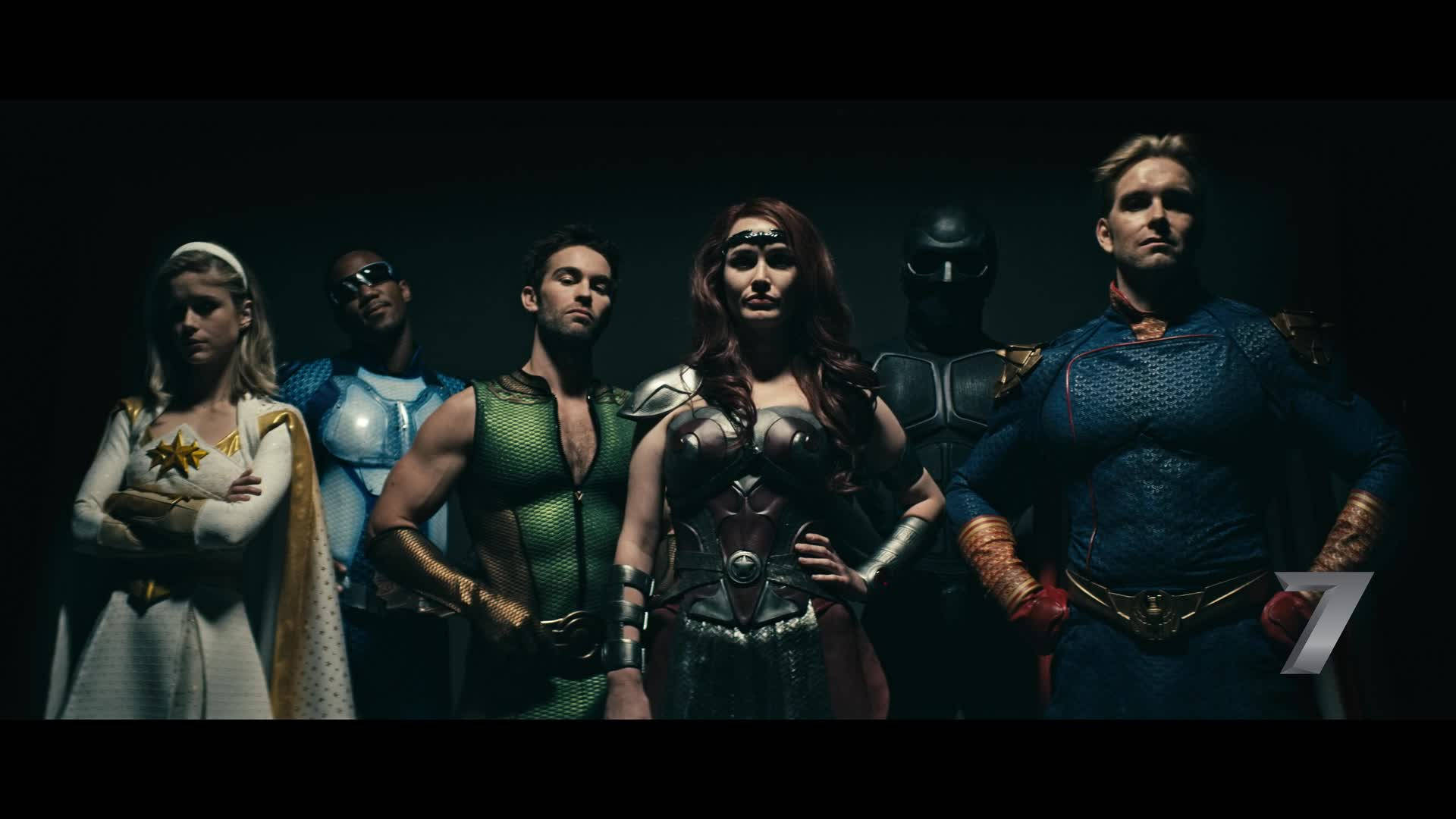 《The Boys》超級英雄陣容 壁紙 — 六位身穿精細服裝的超級英雄在昏暗的攝影棚中自信站立，燈光效果戲劇化。