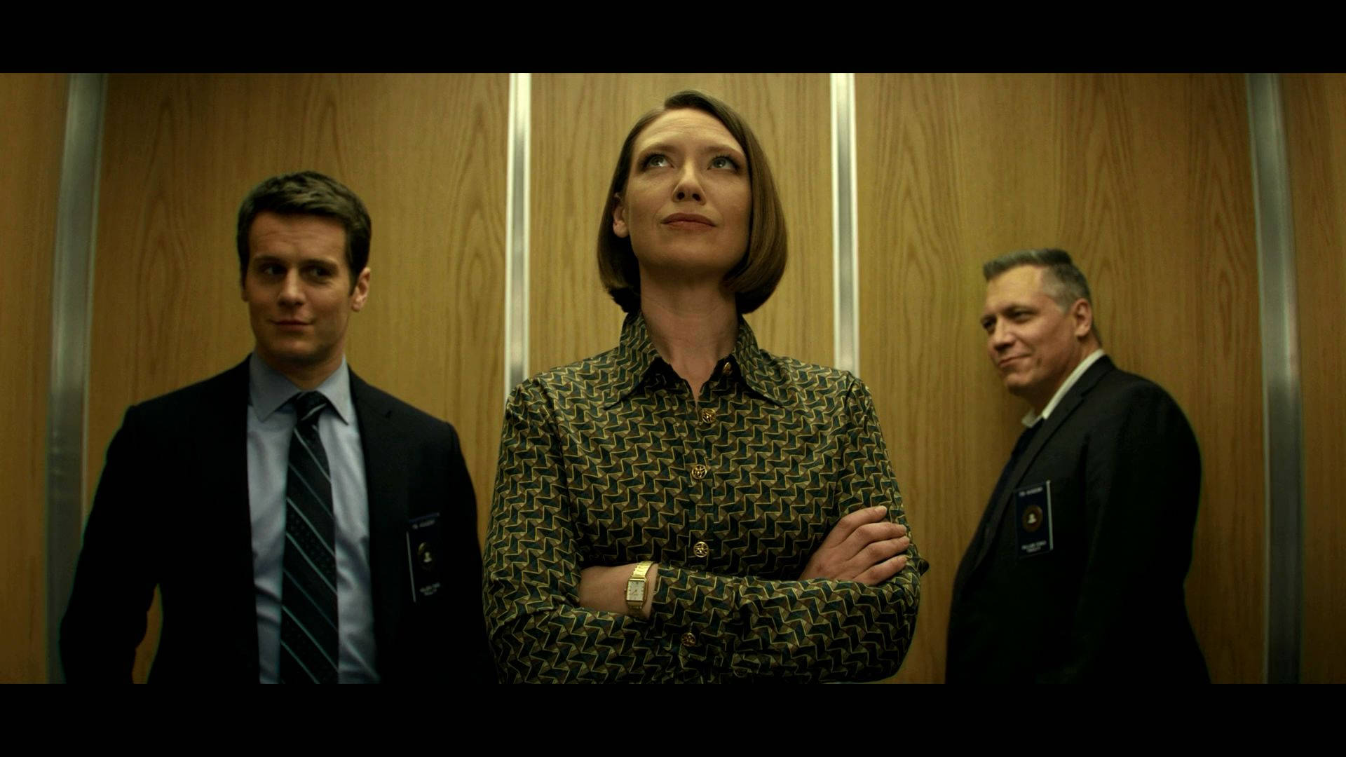 The captivating elevator scene from Mindhunter. 壁紙 — 三位穿著正式服裝的人士站在木質面板的電梯內，表情緊張，雙臂交叉。
