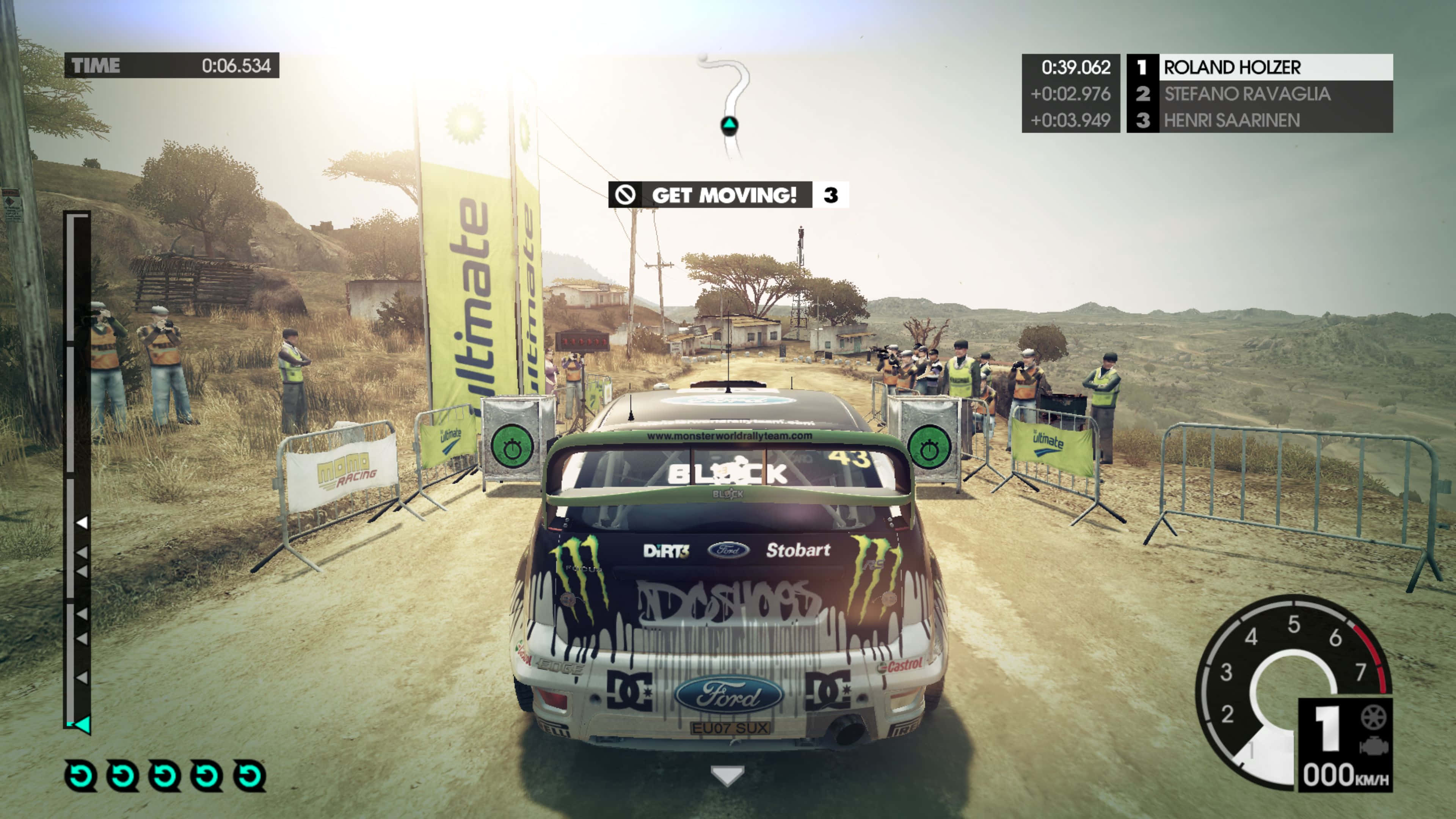 《The Dirt 3》越野競速冒險 壁紙 — 一架帶有Monster Energy貼紙的福特拉力賽車，在明亮的日光下，沿著一條塵土飛揚、兩旁有觀眾和護欄的鄉村道路飛馳。