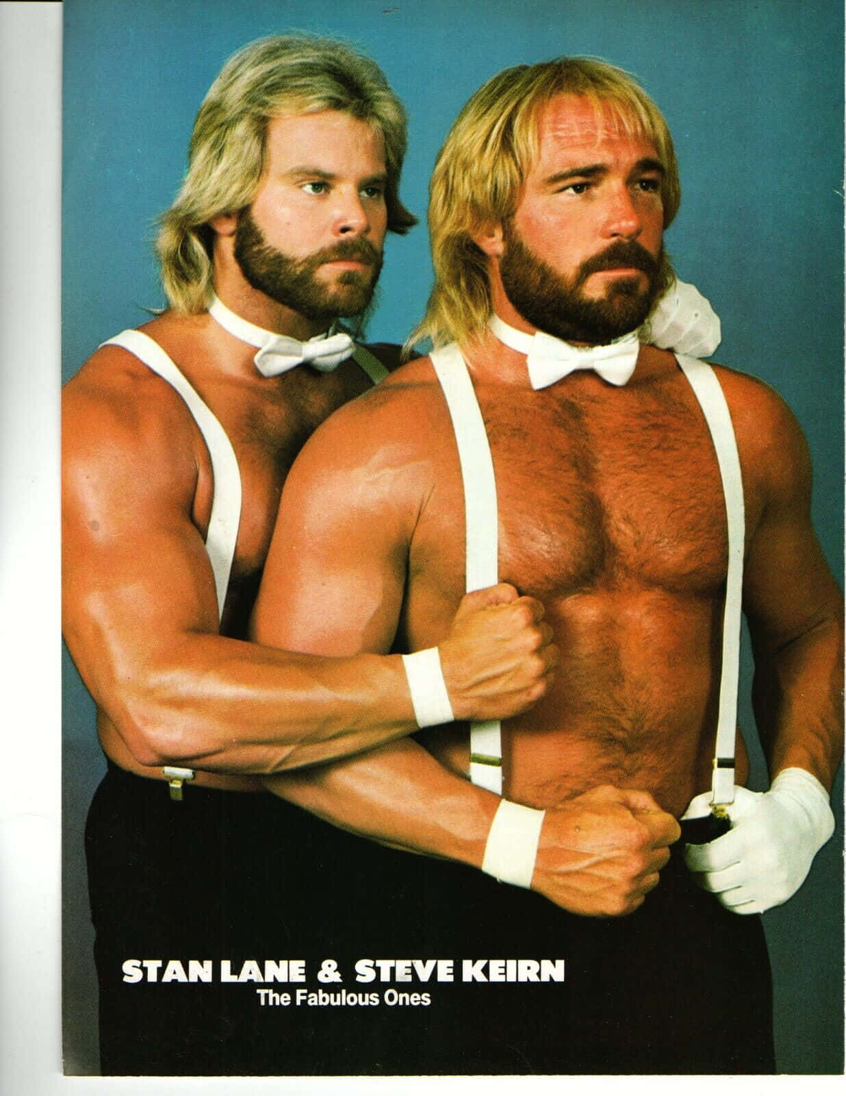 The Fabulous Ones：史丹·萊恩與史蒂夫·基恩 壁紙 — 兩名金髮鬍鬚的肌肉男在藍色背景前穿著白色吊帶和蝴蝶結領結。