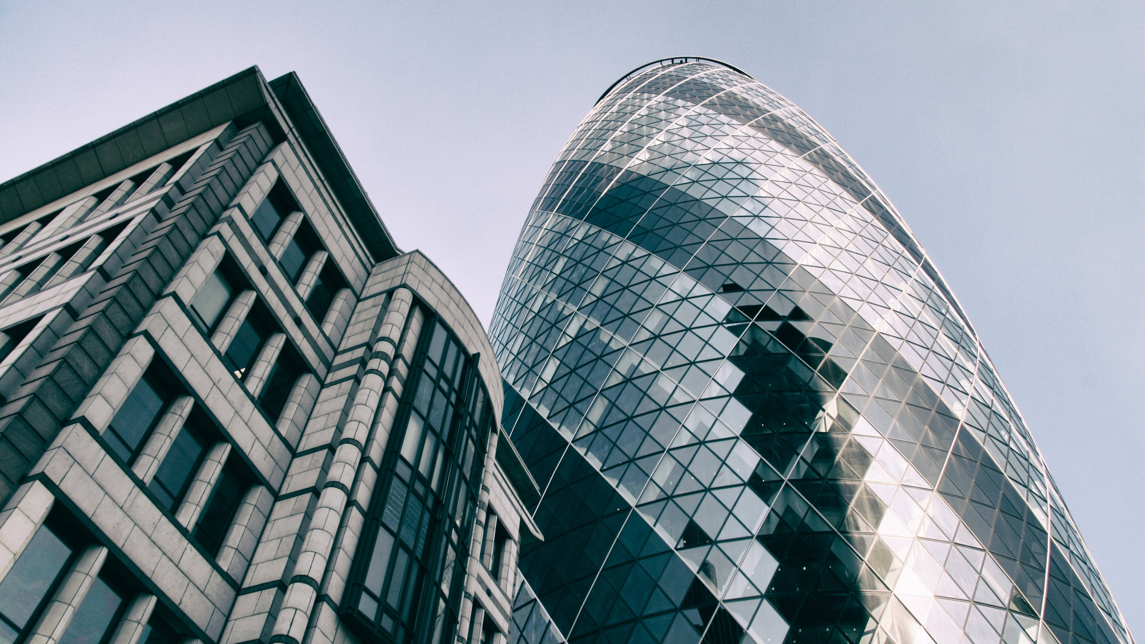 The Gherkin 現代建築 壁紙 — 低角度拍攝一座時尚玻璃摩天大樓，幾何圖案反射天空，旁邊是一座現代化有角建築。