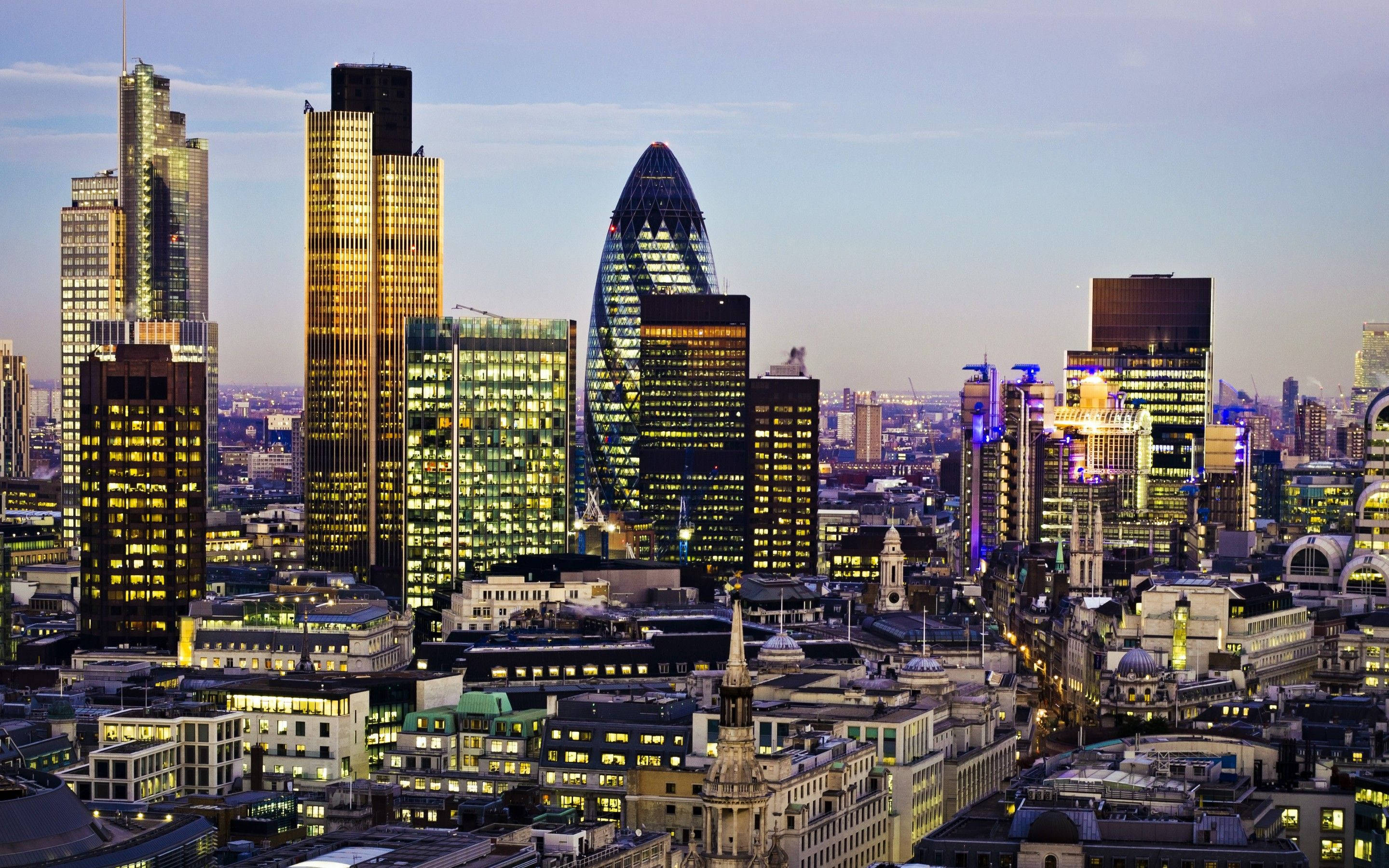 The Gherkin 與倫敦天際線 壁紙 — 倫敦天際線在黃昏時分，摩天大樓和歷史建築在柔和的紫色天空下閃閃發光。